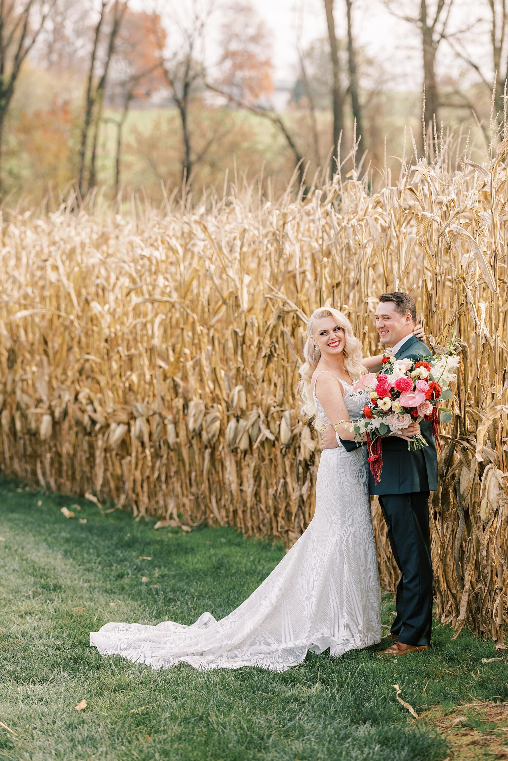 groom hugs bride around waist holding pink and white bouquet at Osbornia Farm