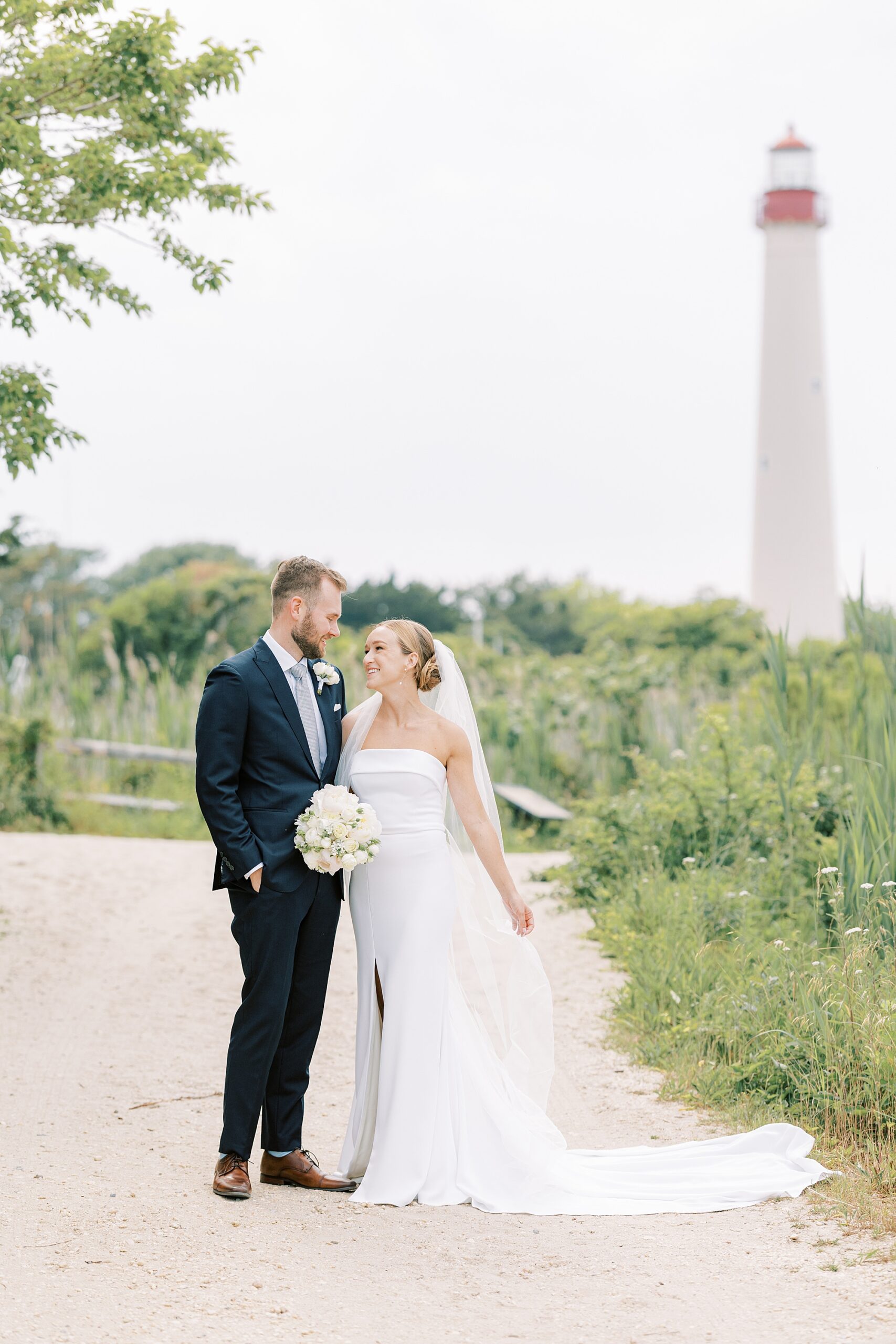 bride and groom hug in front of Cape May lighthouse