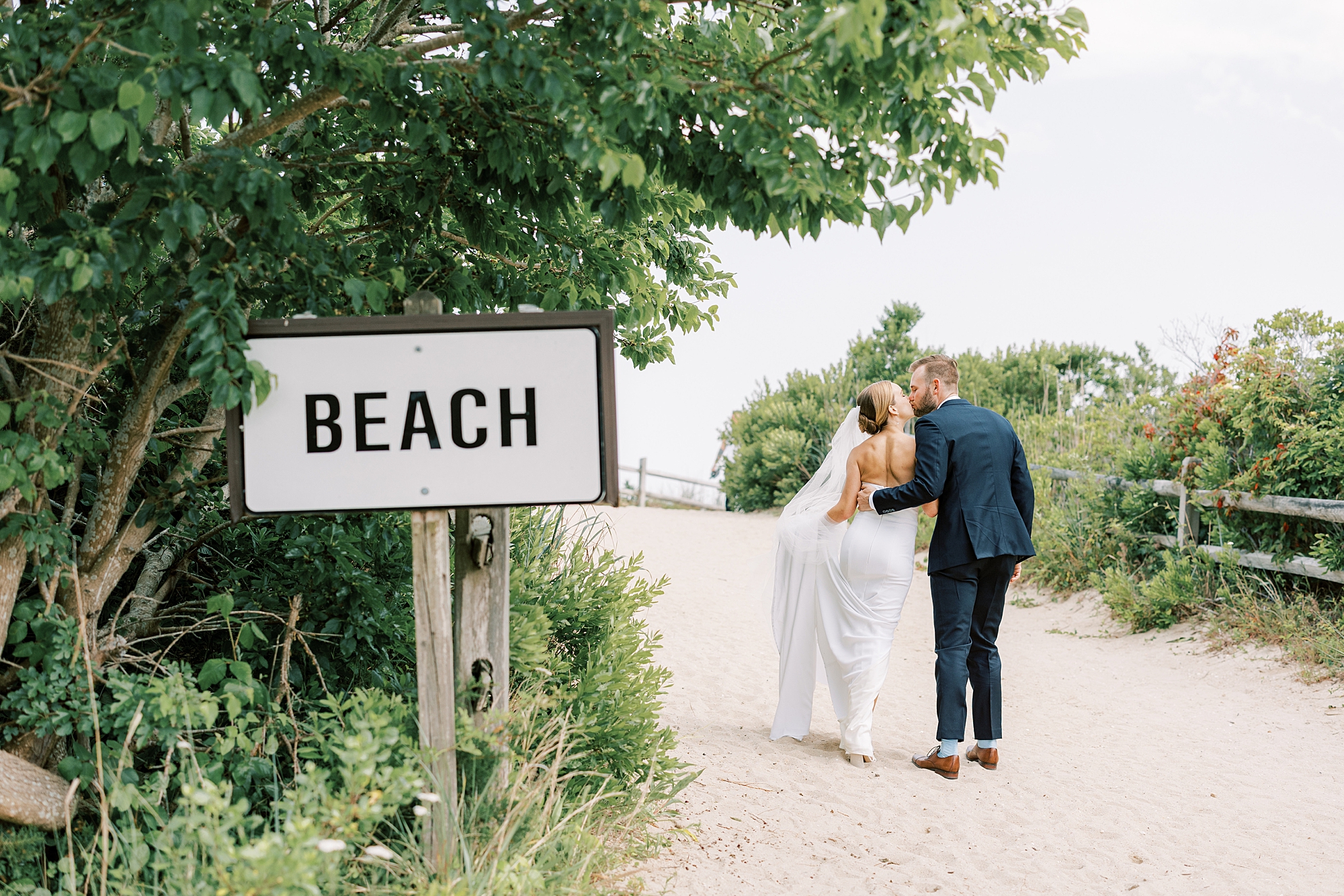 bride and groom hug near beach sign by Cape May lighthouse