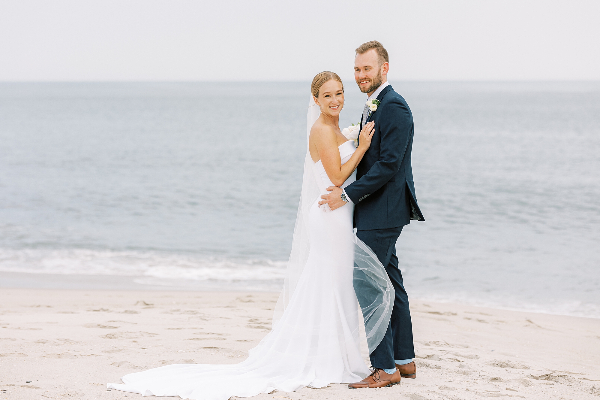 bride hugs groom laying hand on his lapel during Cape May beach wedding portraits 