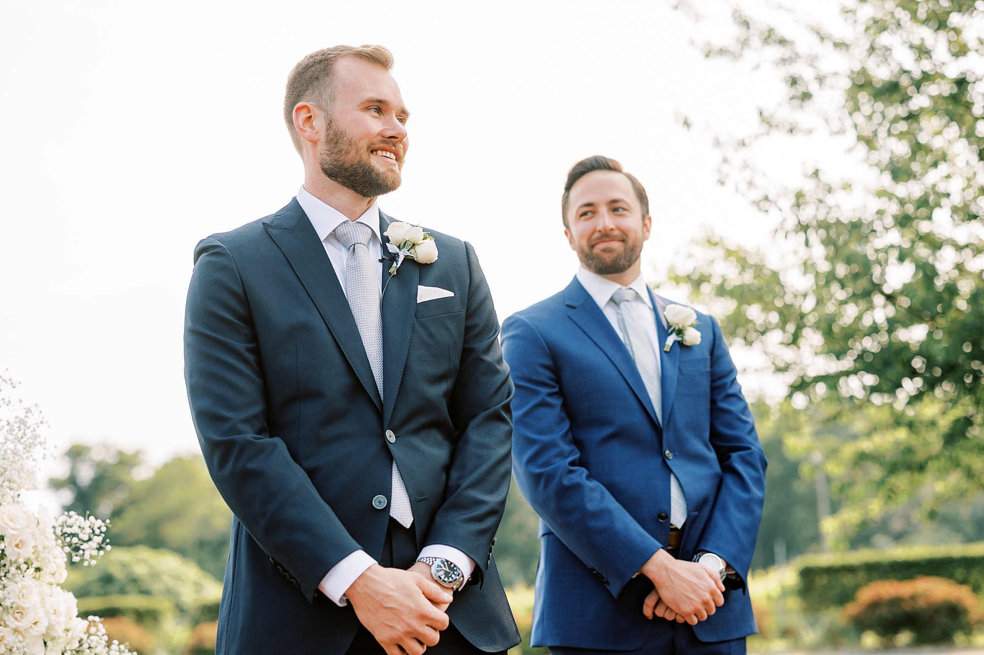groomsman in navy suit looks at groom during wedding ceremony at Willow Creek Winery