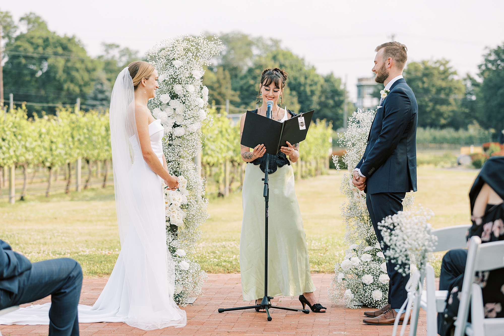 bride and groom listen to officiant during wedding ceremony at Willow Creek Winery with white floral arch 