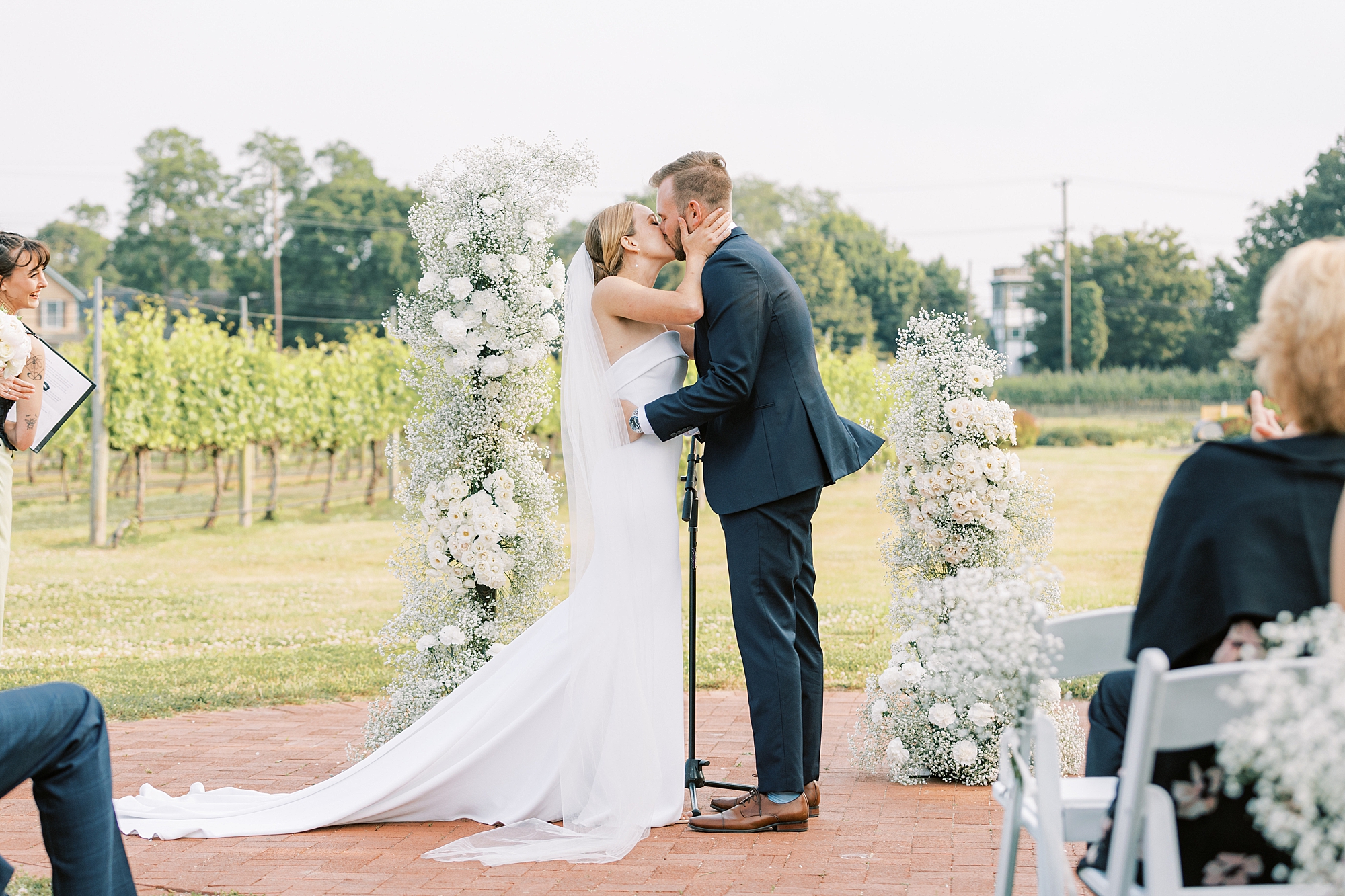 bride and groom kiss after wedding ceremony at Willow Creek Winery in front of white flower arches 