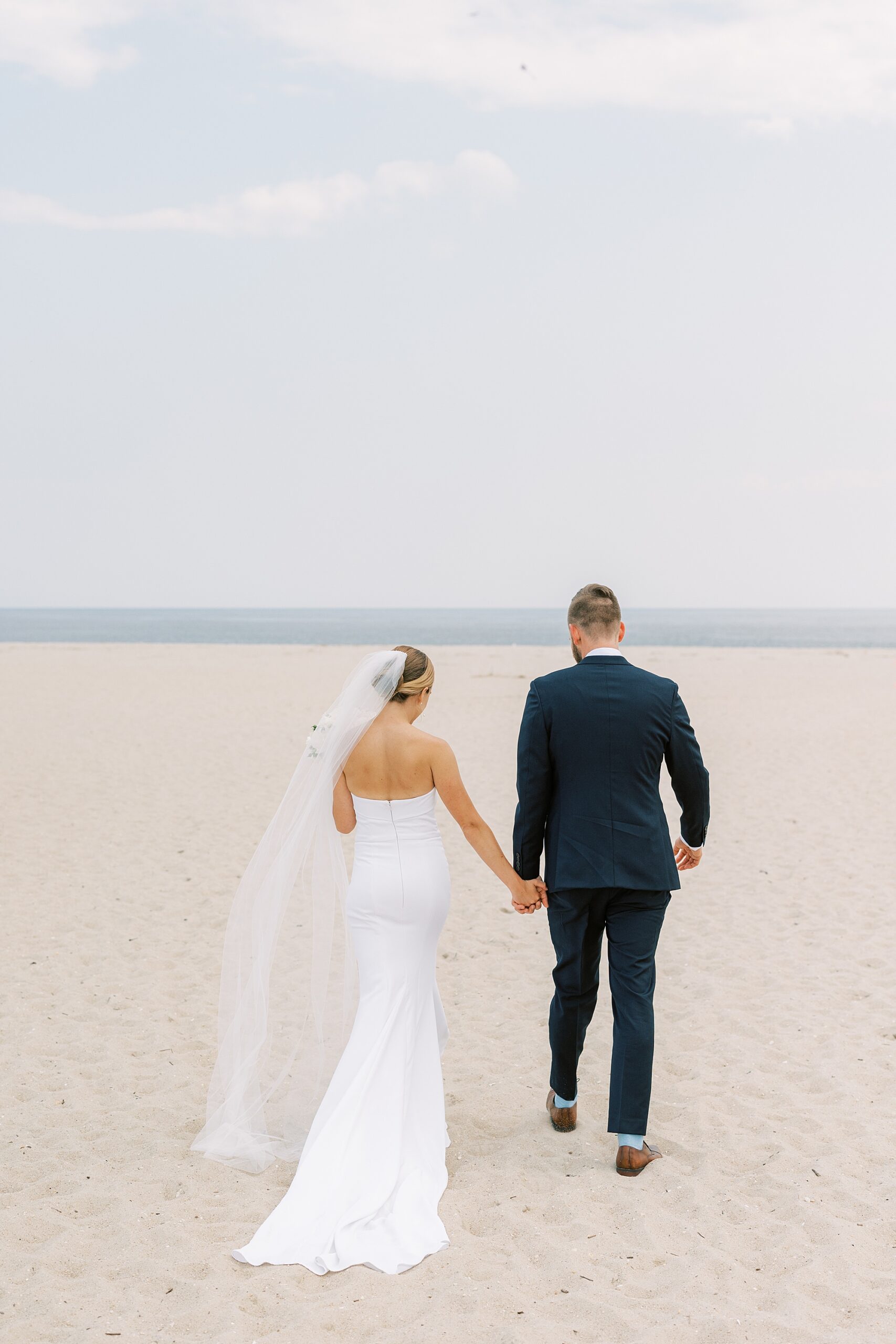 bride and groom hold hands walking on Cape May NJ beach