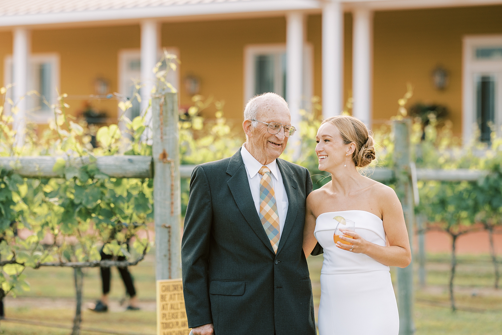 bride hugs grandfather smiling at him on edge of vines at Willow Creek Winery