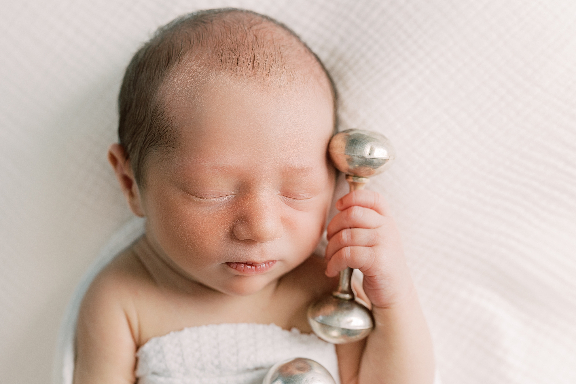 baby holds silver rattle by head during Chadds Ford PA newborn session