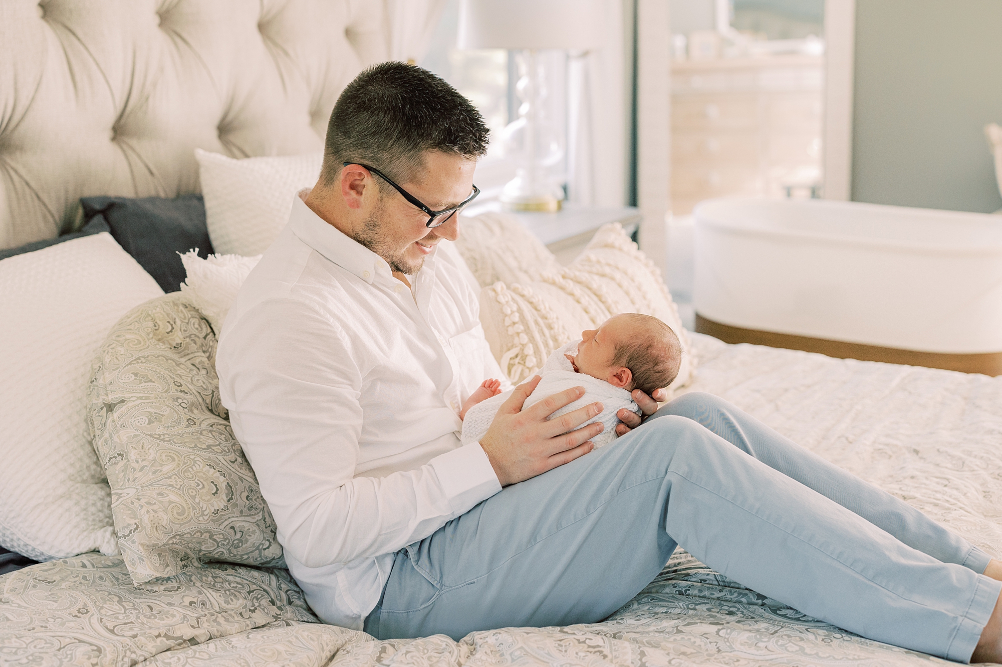 dad holds son on thighs siting on the bed during Chadds Ford PA newborn session