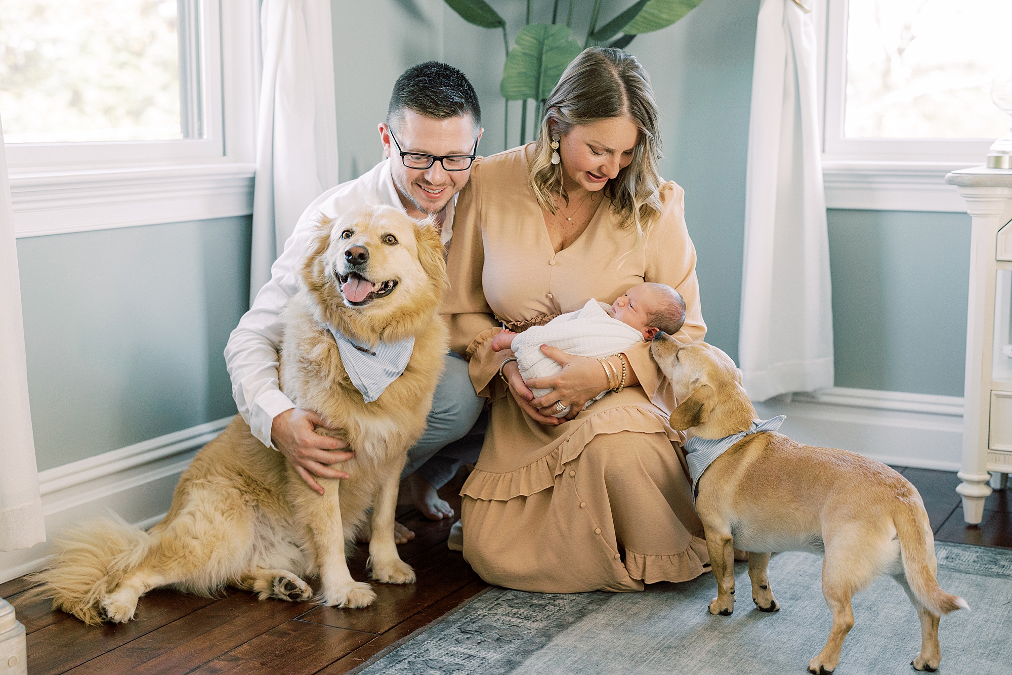parents snuggle with two dogs and newborn son in nursery of Chadds Ford PA home