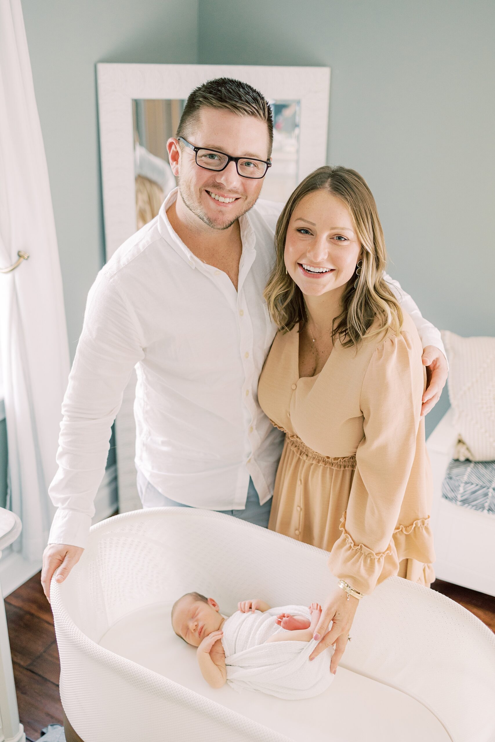 parents pose by bassinet with newborn son inside 
