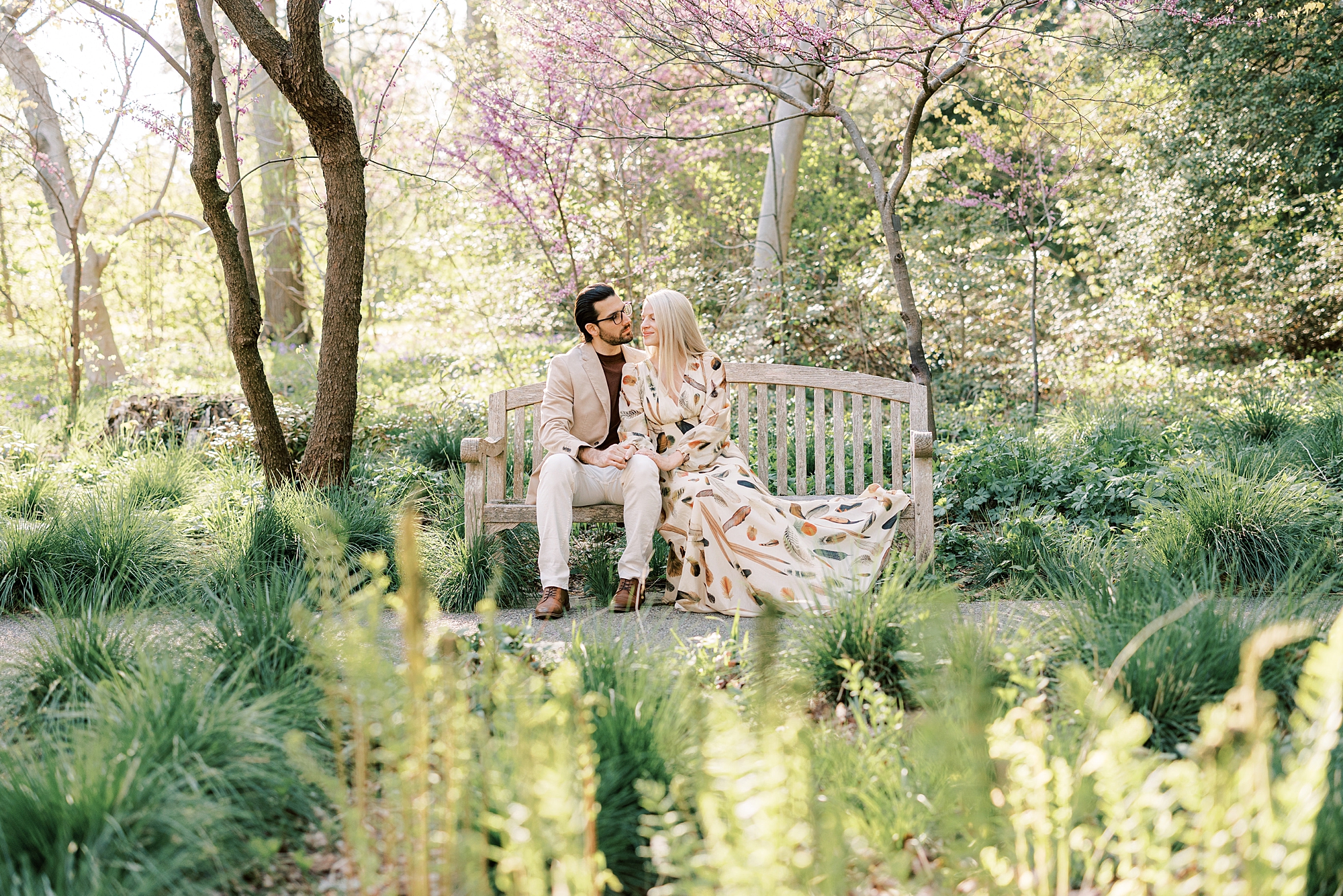 engaged couple sits on wooden bench inside Longwood Gardens during spring engagement photos