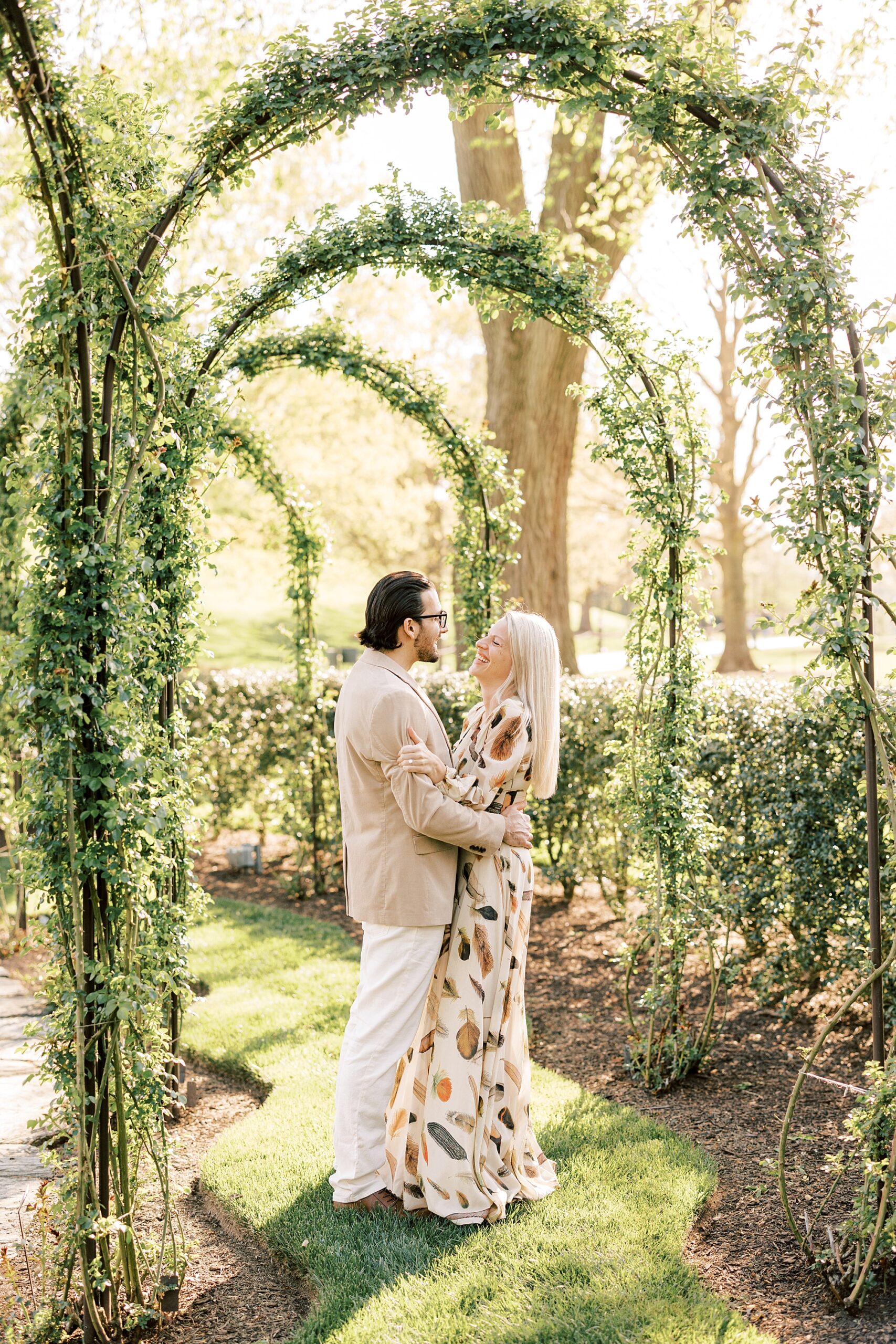 engaged couple hugs under greenery arbor during spring engagement session at Longwood Gardens