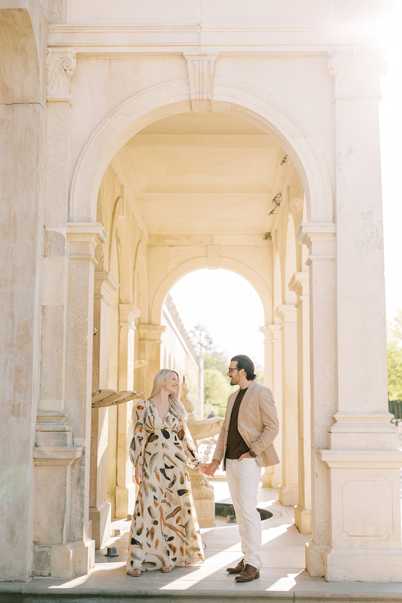 engaged couple holds hands walking through arches at Longwood Gardens 