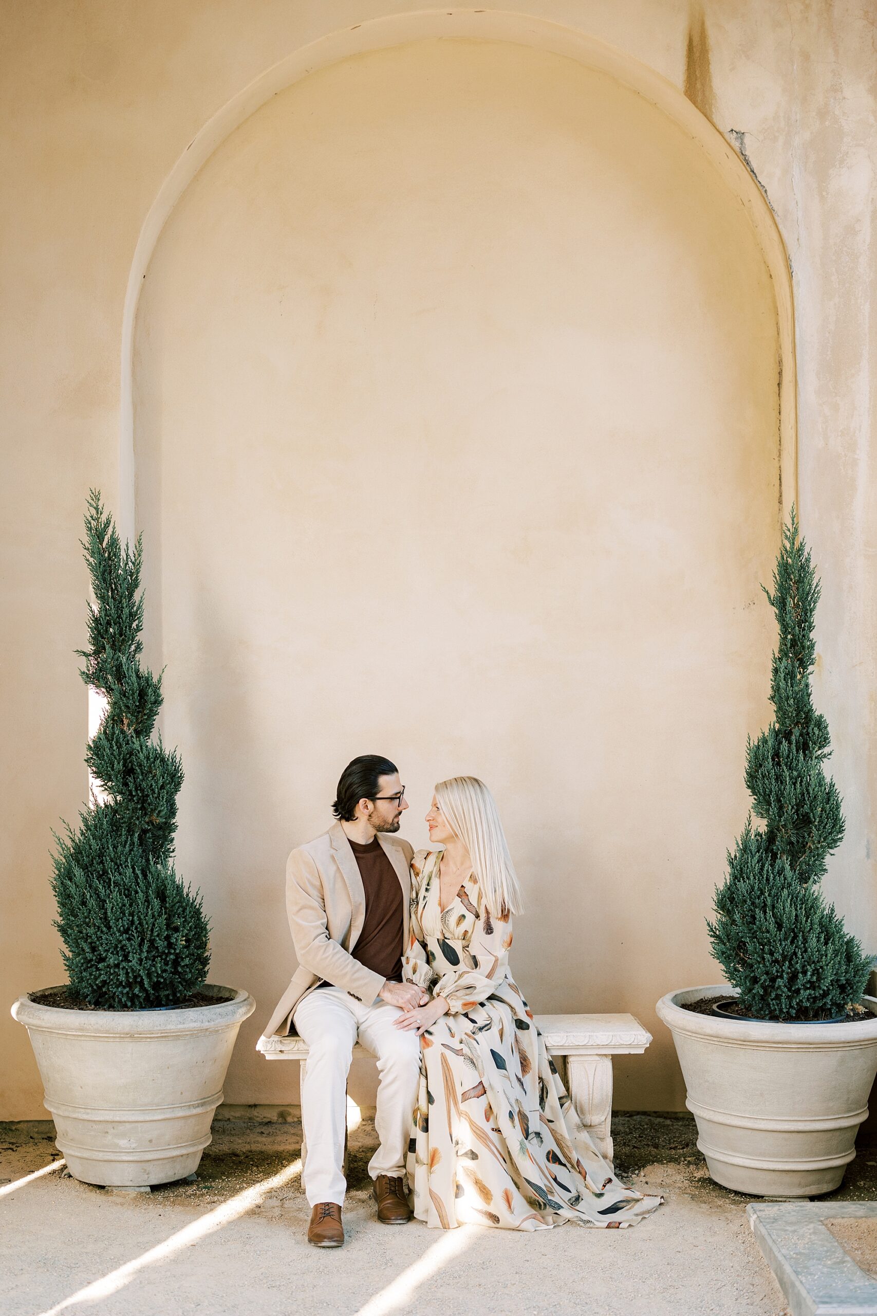 man and woman sit in front of tan wall during spring engagement session at Longwood Gardens