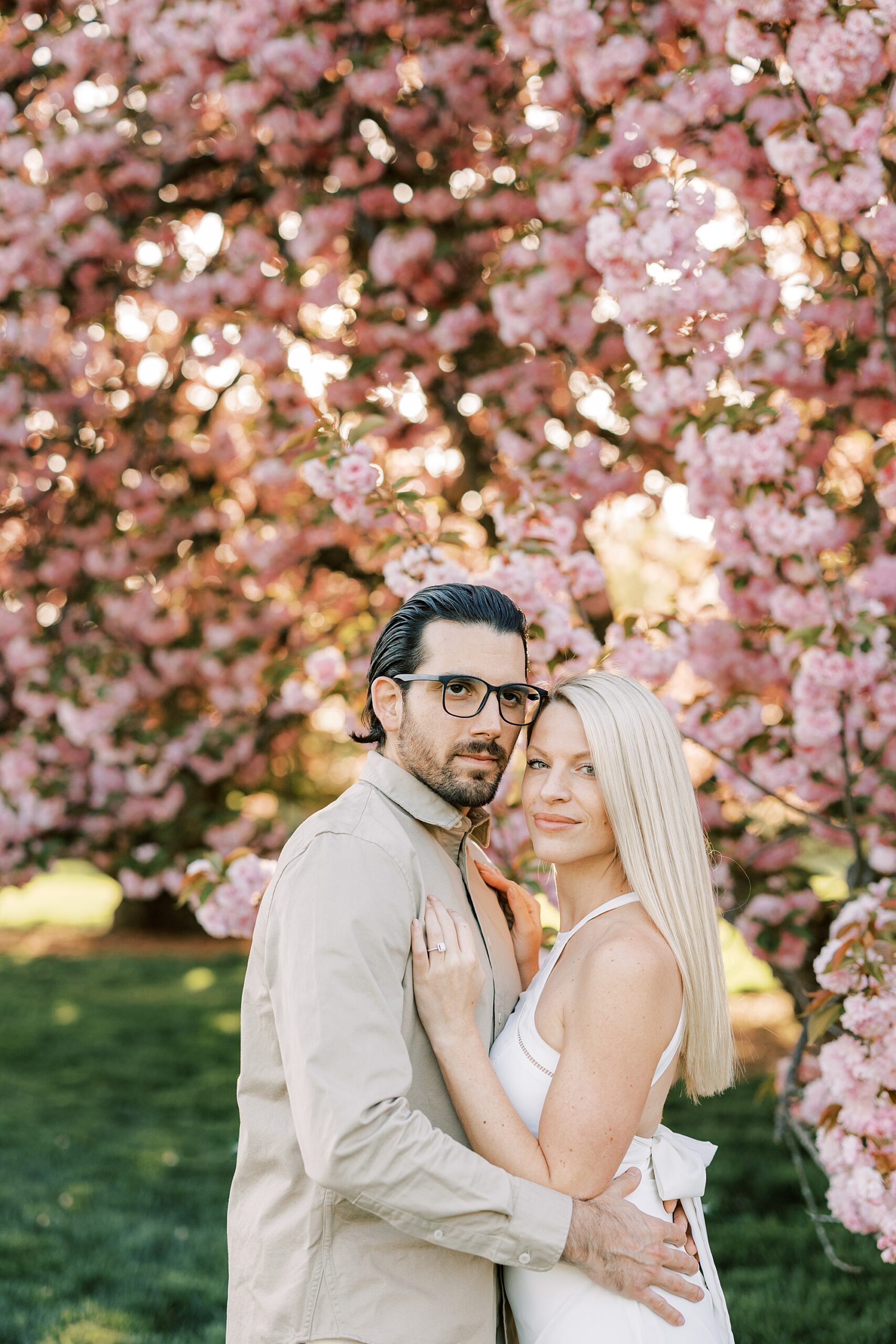 man and woman hug in front of pink cherry blossom tree at Longwood Gardens