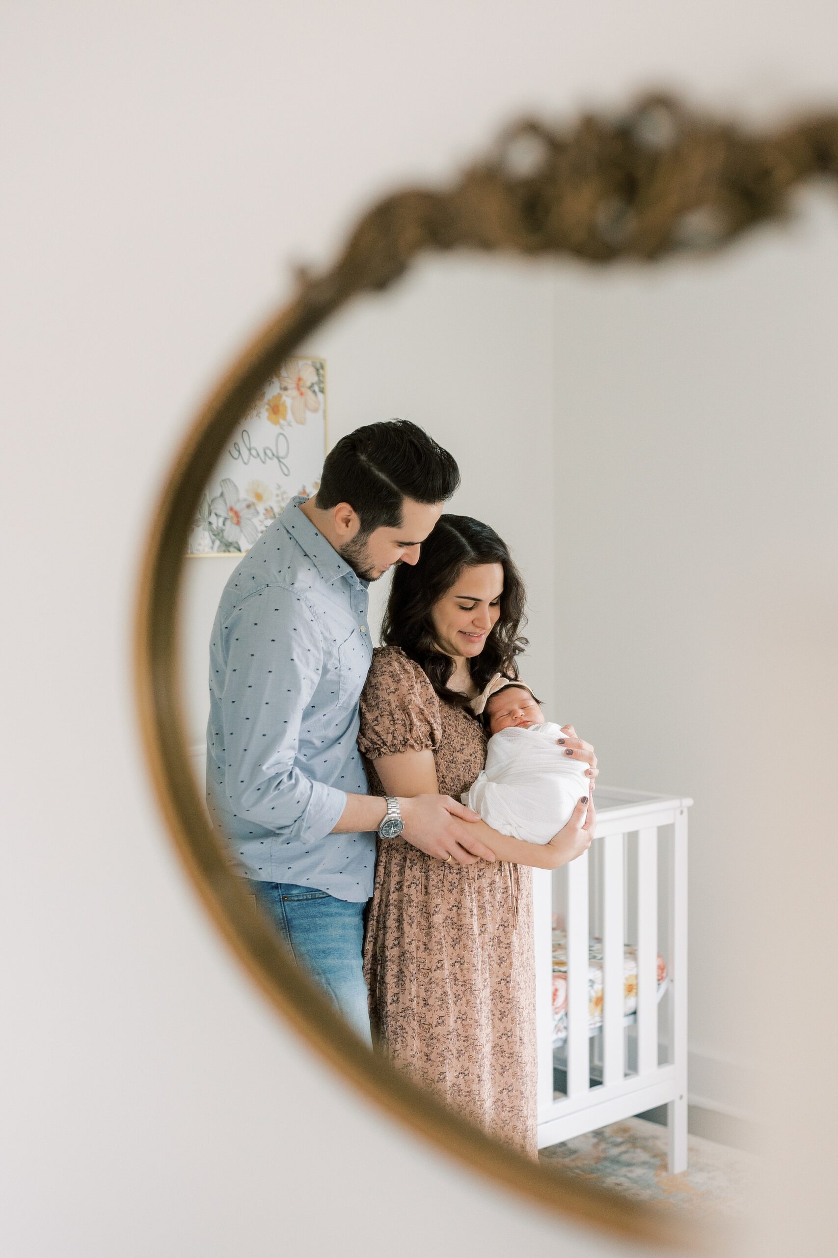 reflection of wife and husband holding newborn daughter in gold rimmed mirror