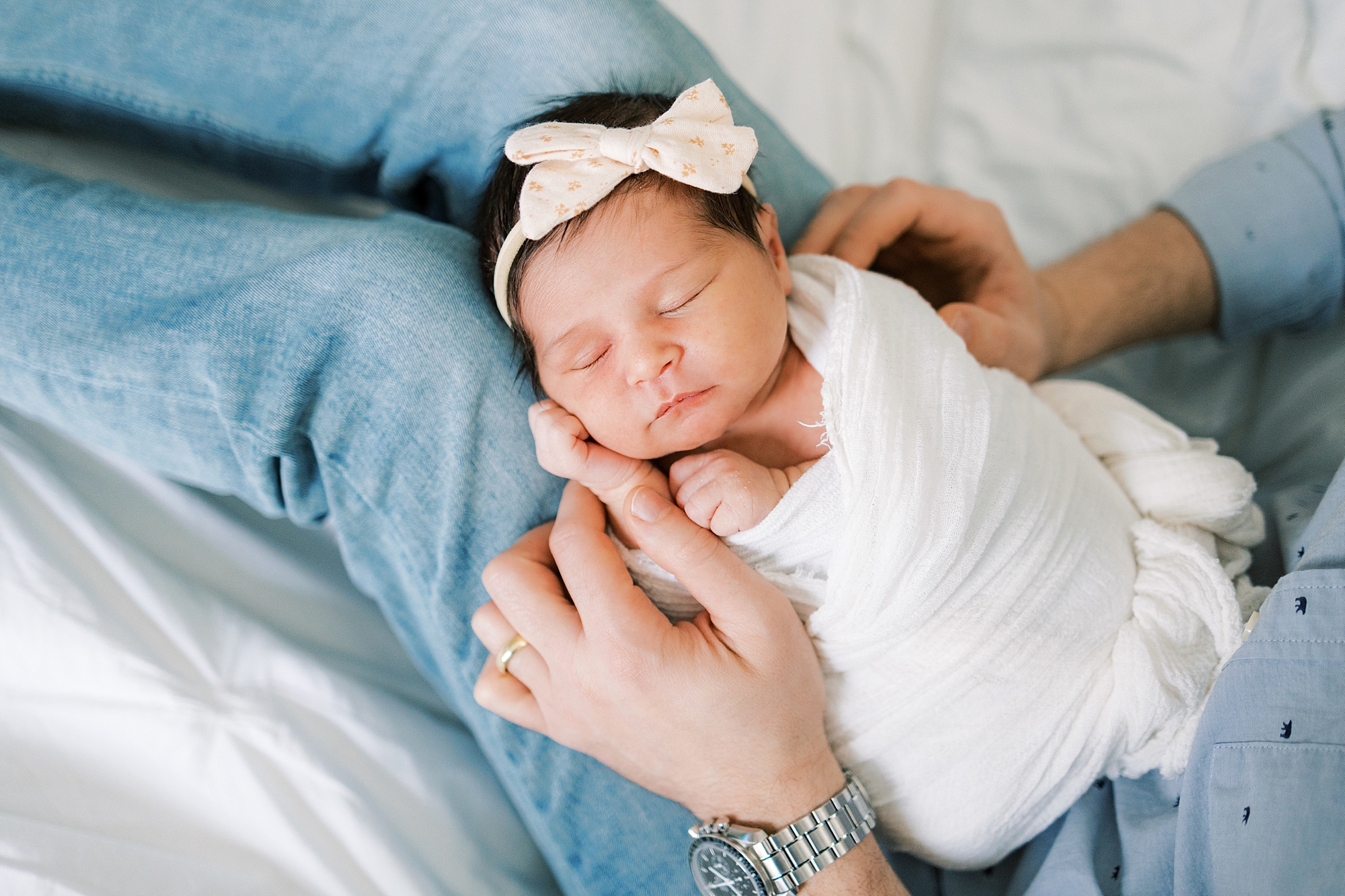 baby girl in white wrap lays on dad's legs on bed during newborn portraits at home in Media PA