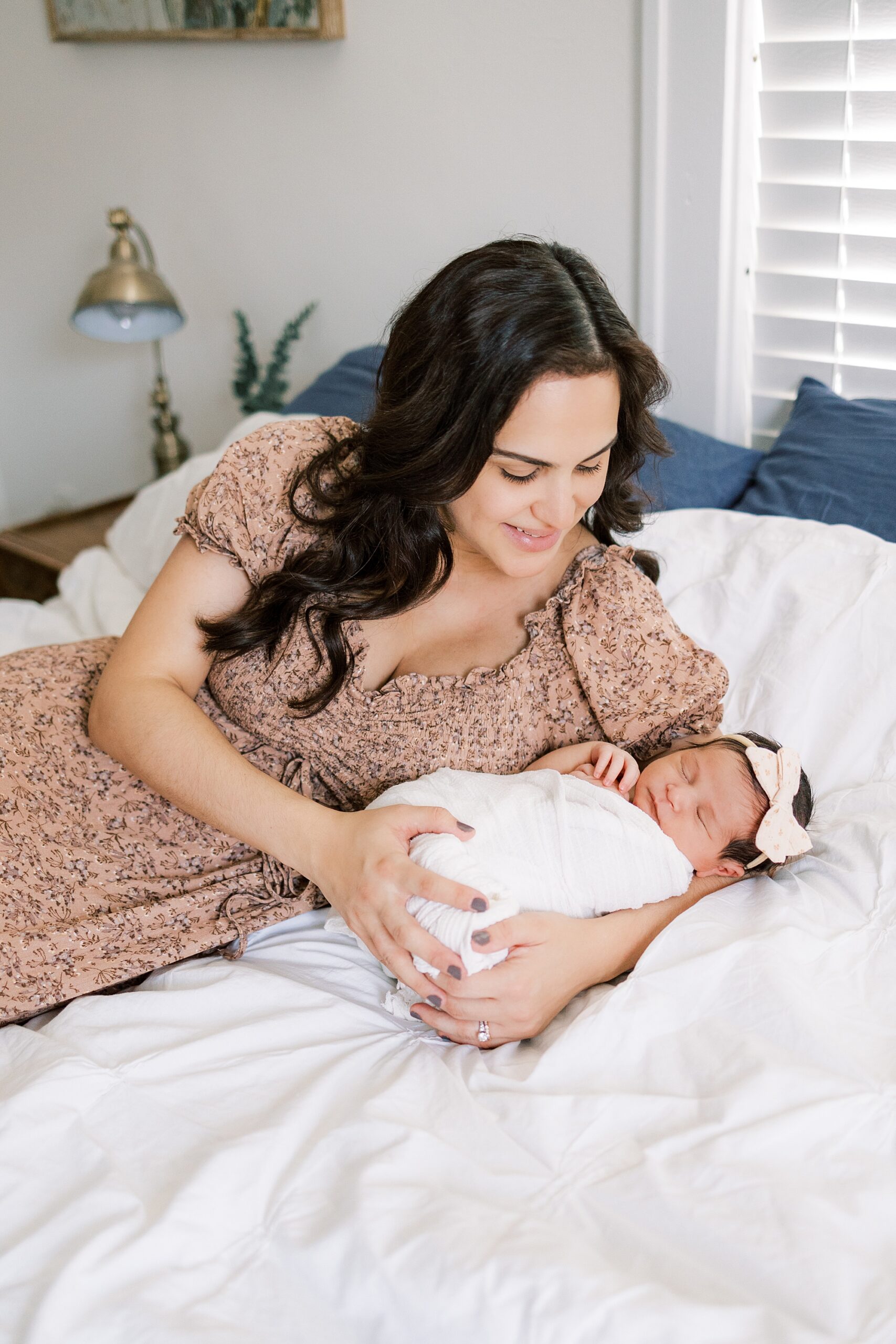mom lays on bed holding newborn daughter during newborn portraits at home in Media PA