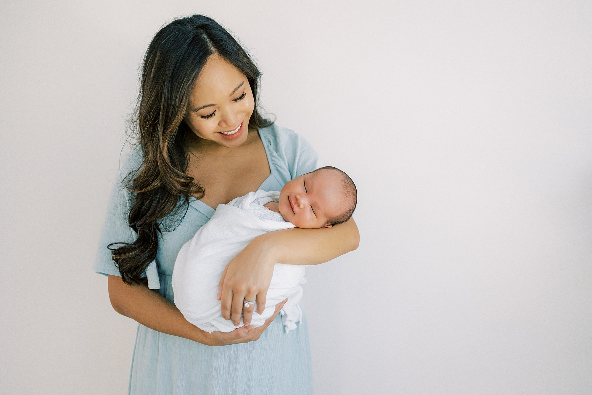 mother in light blue dress  holds son in white wrap during newborn session in Cherry Hill NJ