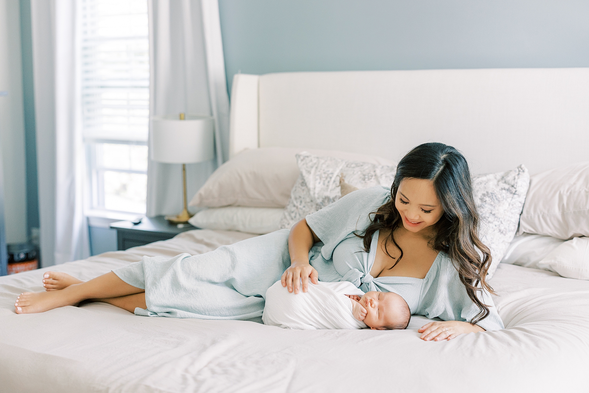 mom lays on bed with baby boy in white wrap during newborn session in Cherry Hill NJ