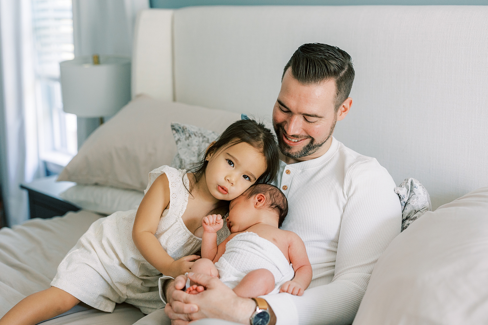 dad holds toddler girl and newborn son on lap during newborn session in Cherry Hill NJ