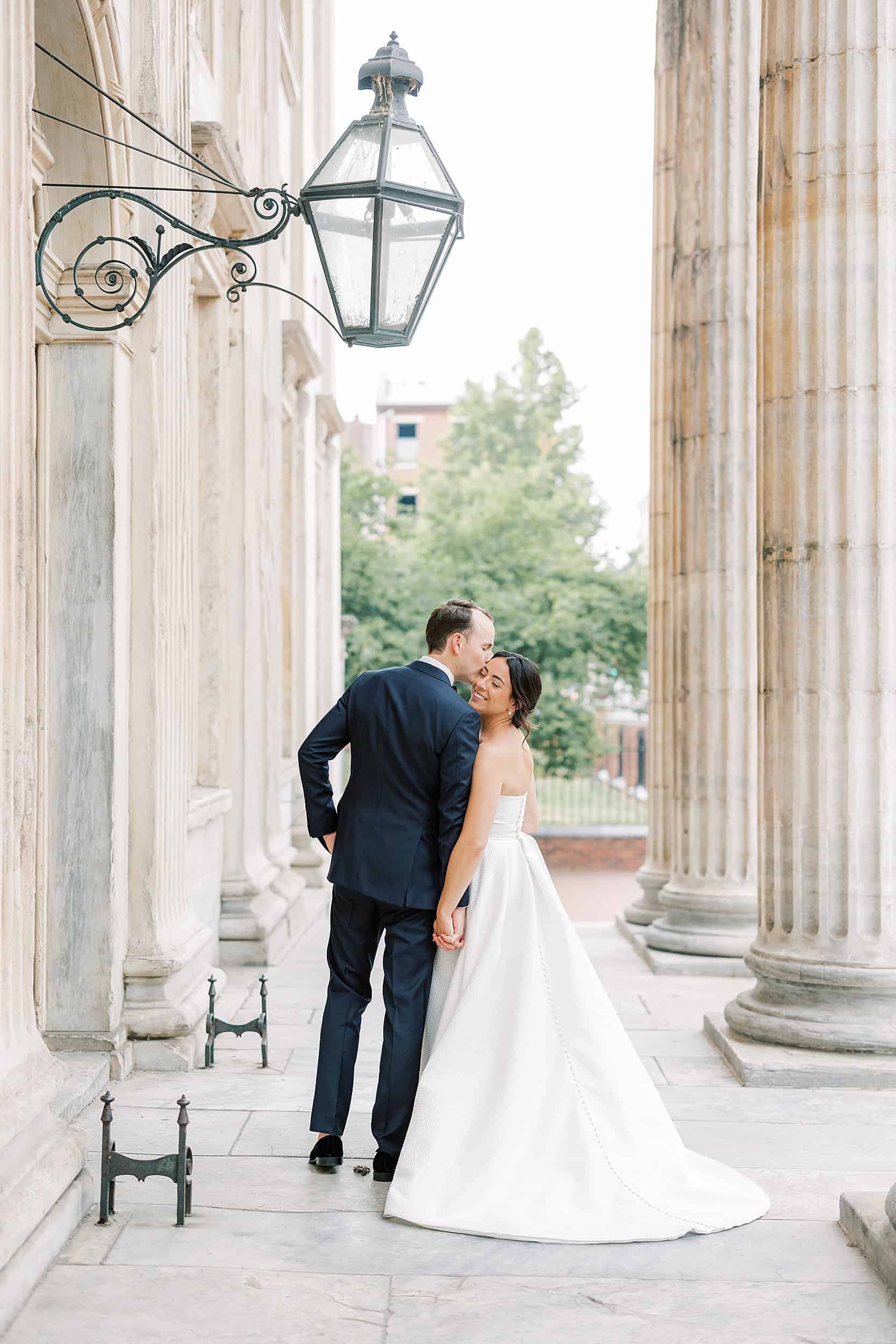 groom kisses his wife on the cheek as they walk away at Philadelphia's second bank