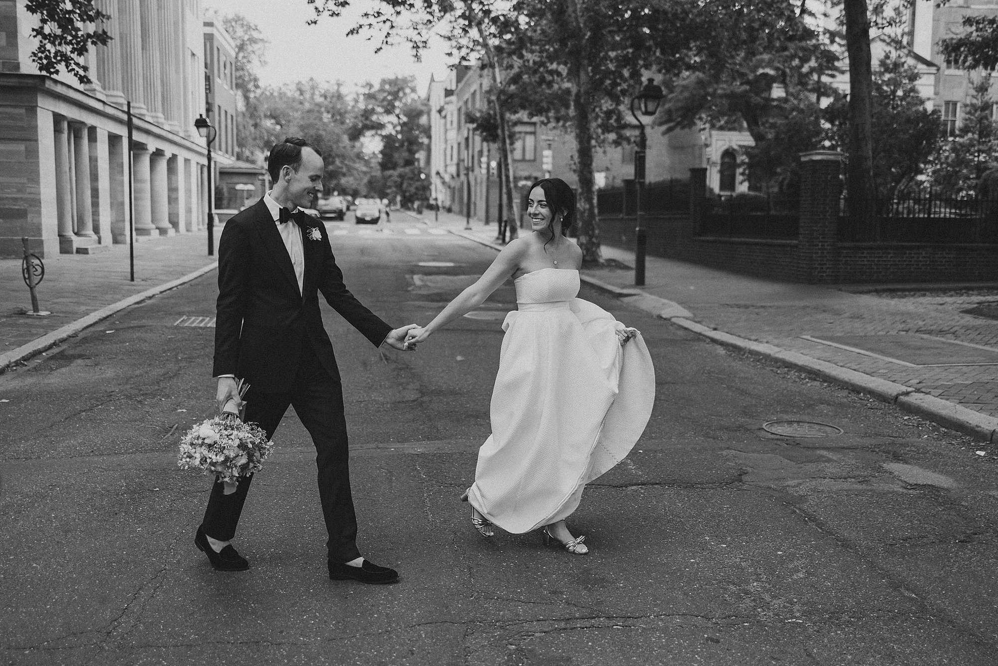 bride smiles back at her groom while she pulls him across the Philadelphia city streets