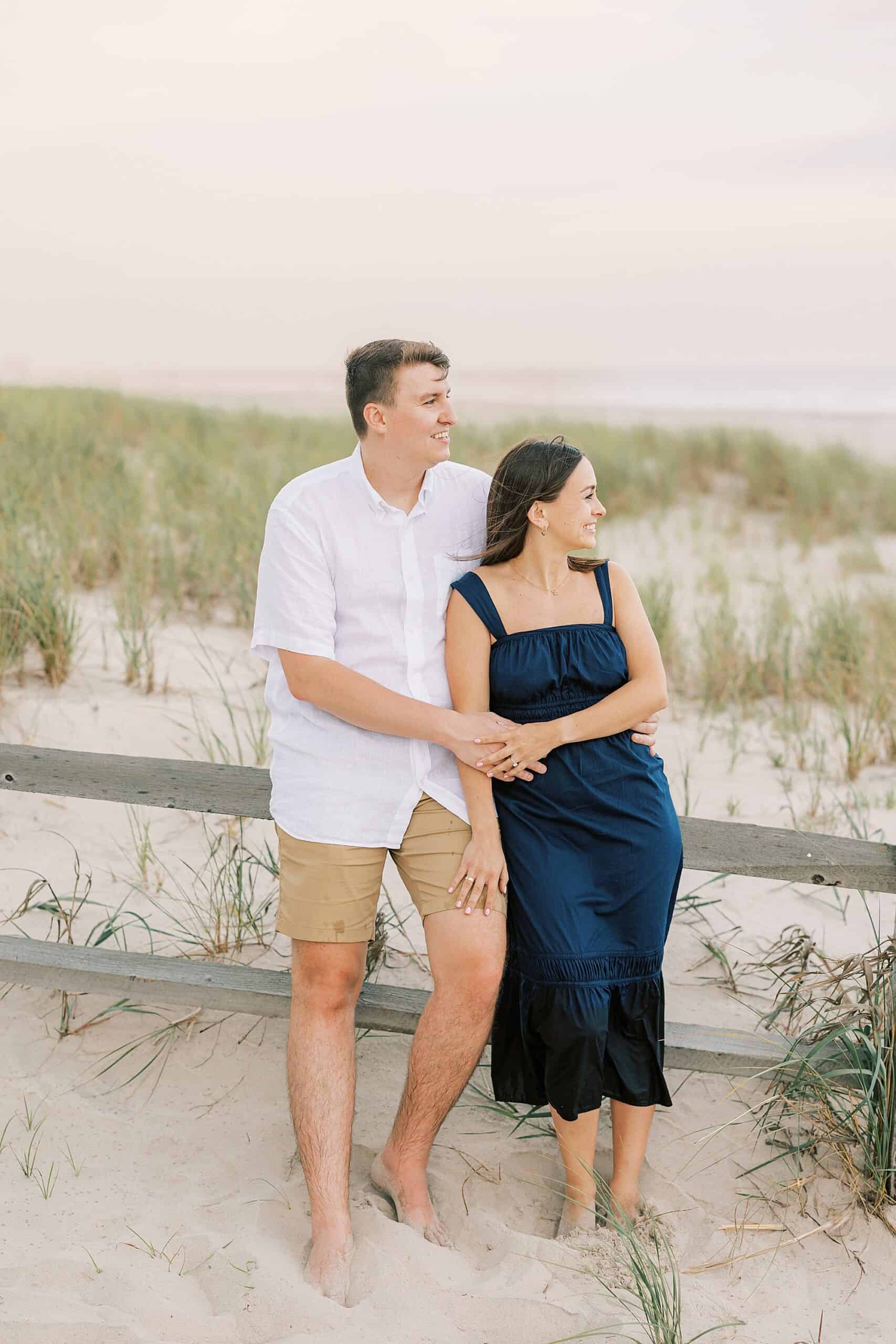 engaged couple sits together on the dunes overlooking a beautiful sunset during their Ocean City NJ Engagement Photo Session