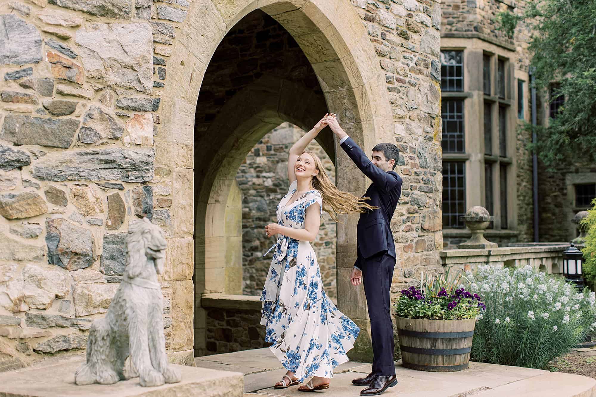 a groom spins his bride in front of a beautiful stone mansion during their engagement photo session at Ridley Creek State Park