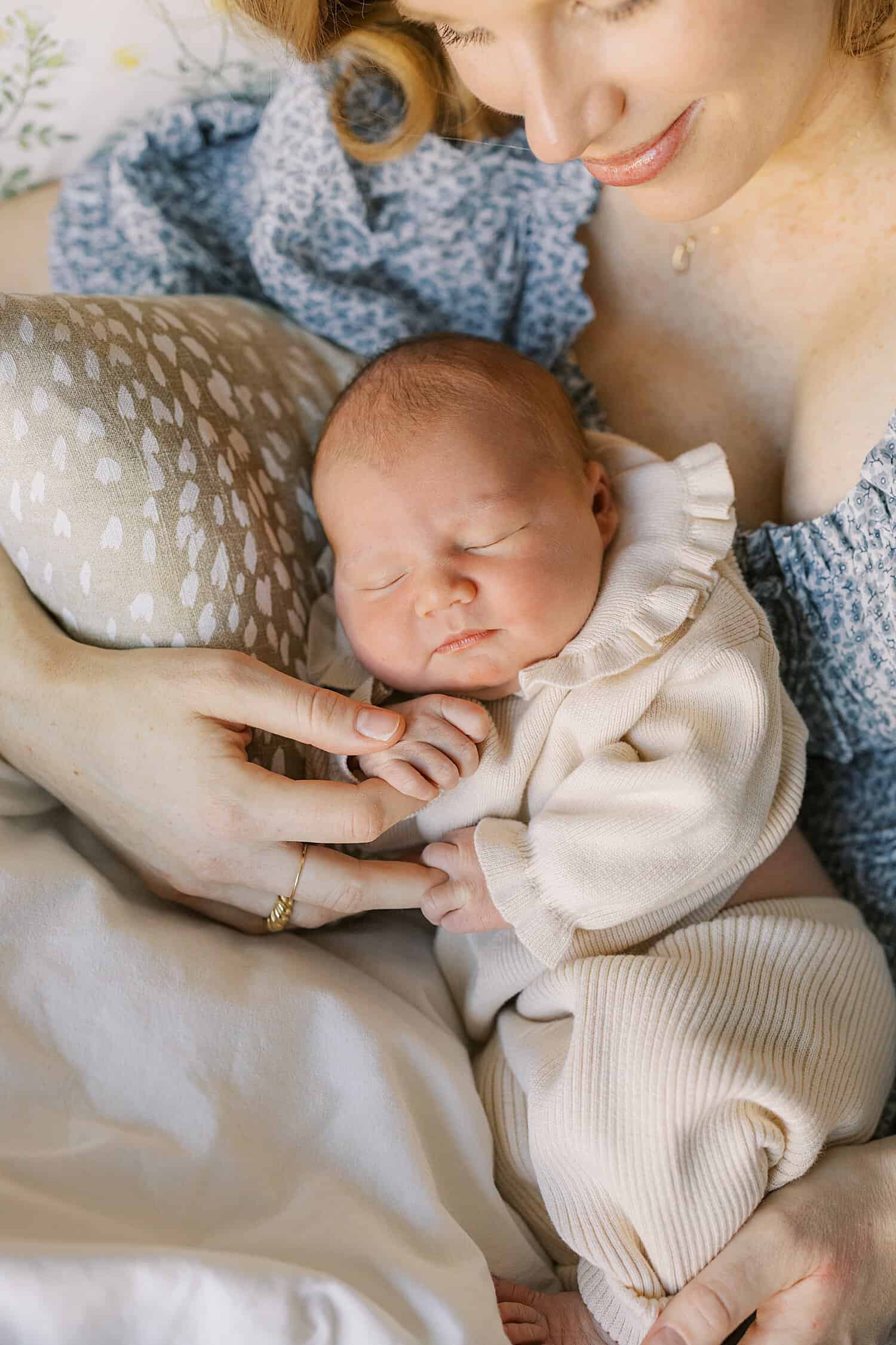 Kennett Square newborn photographer Samantha Jay captures a cozy image of a mother reclined on a bed in a blue floral dress cradling her newborn baby girl while she sleeps