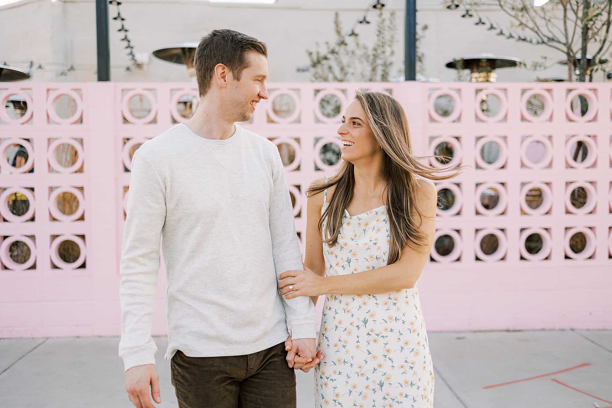 a woman smiles over at her husband with windswept hair and pink breeze blocks behind her