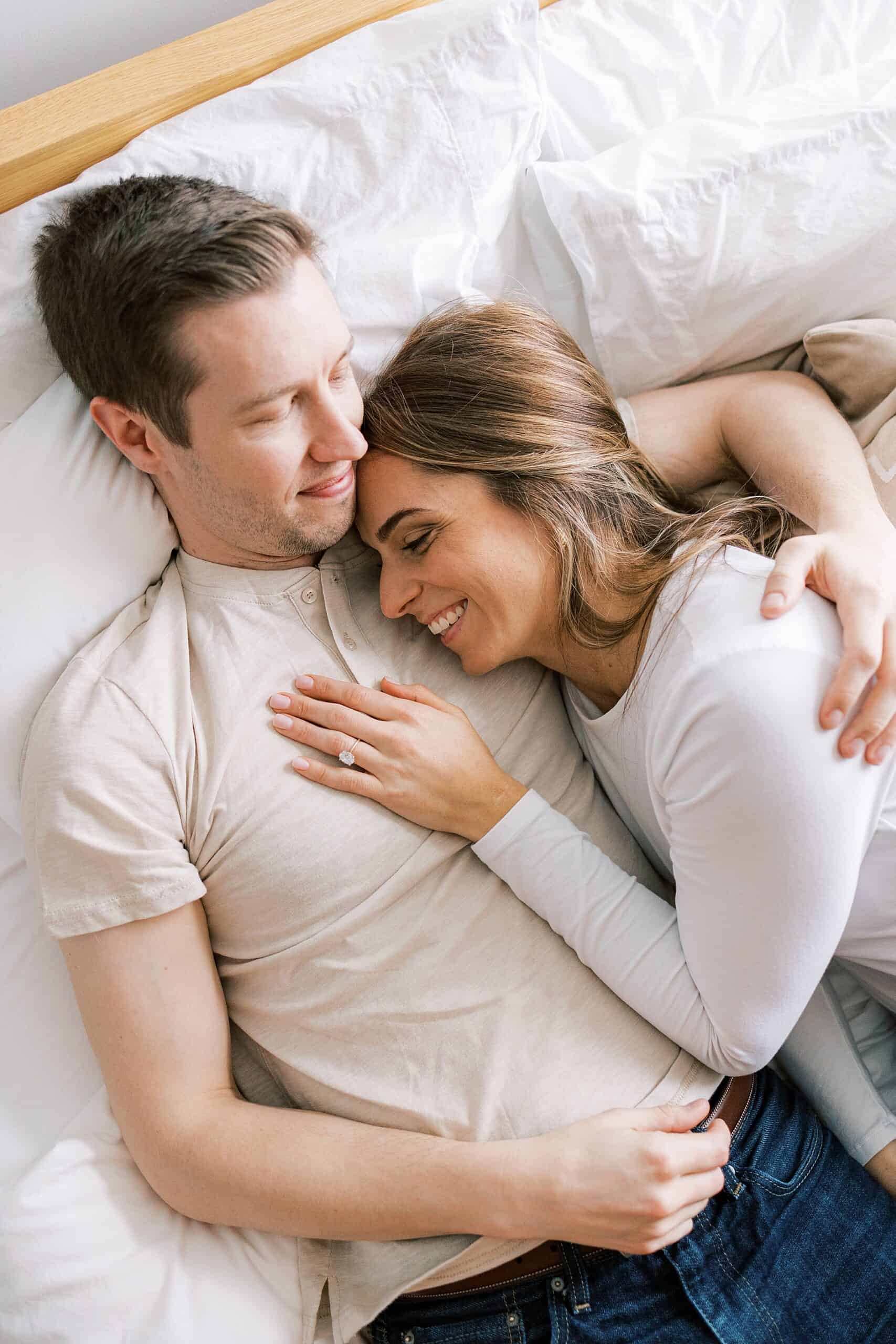 a woman snuggles up to her partner on a bed in snuggly clothing as she brainstorms Valentines Gifts for Men