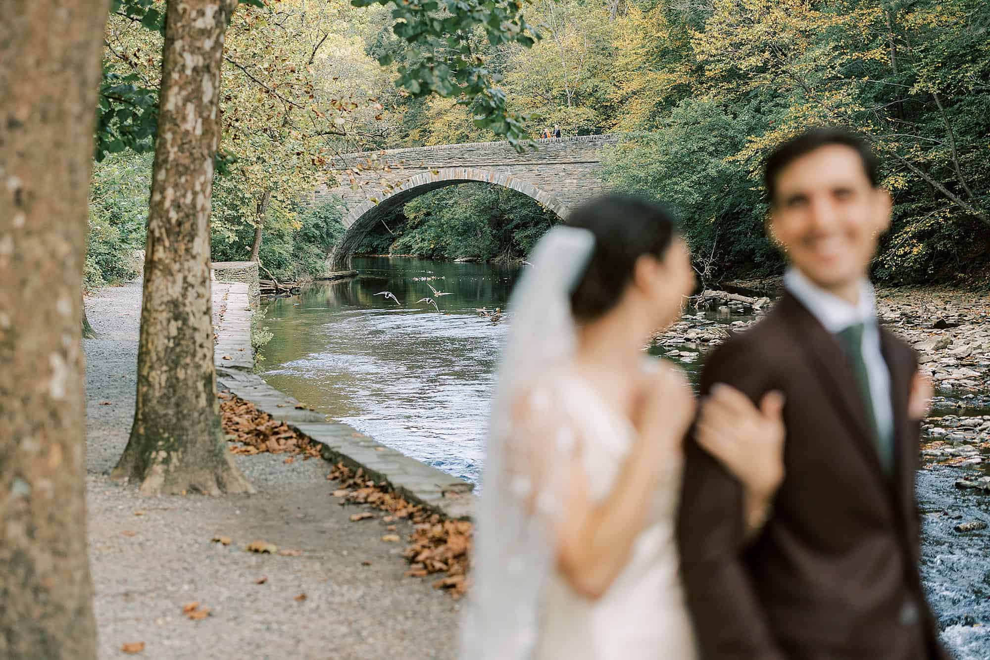 a bride and groom out of focus in the foreground with geese flying over a creek in background at Valley Green Inn