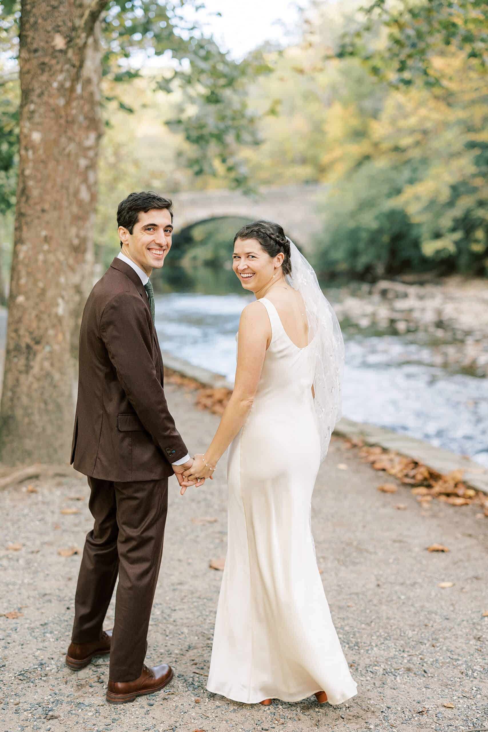 a bride looks over her shoulder as she walks away with her groom on a gravel path at Valley Green Inn on their wedding day