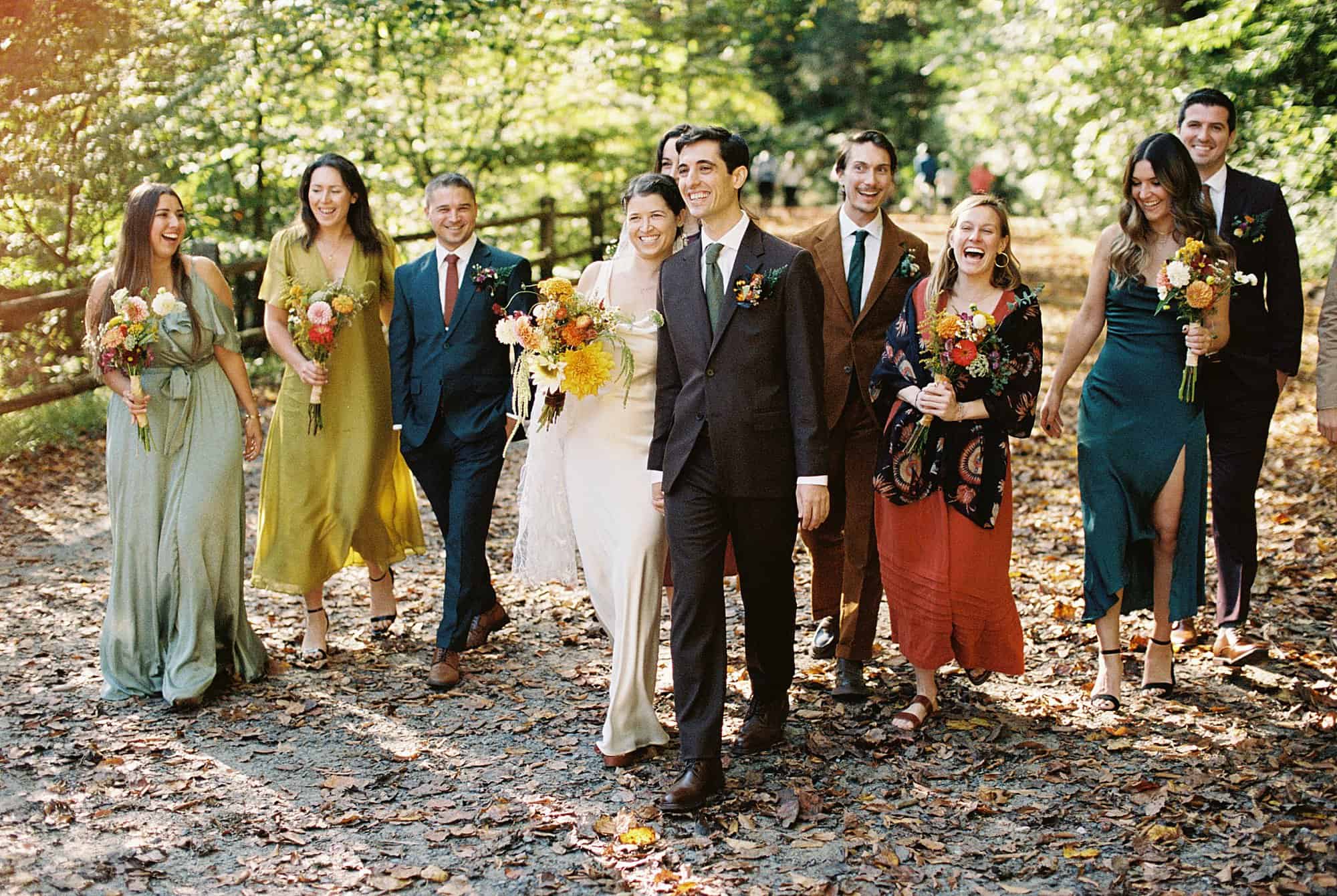 a bride and groom walk toward the camera surrounded by their wedding party in jewel tones