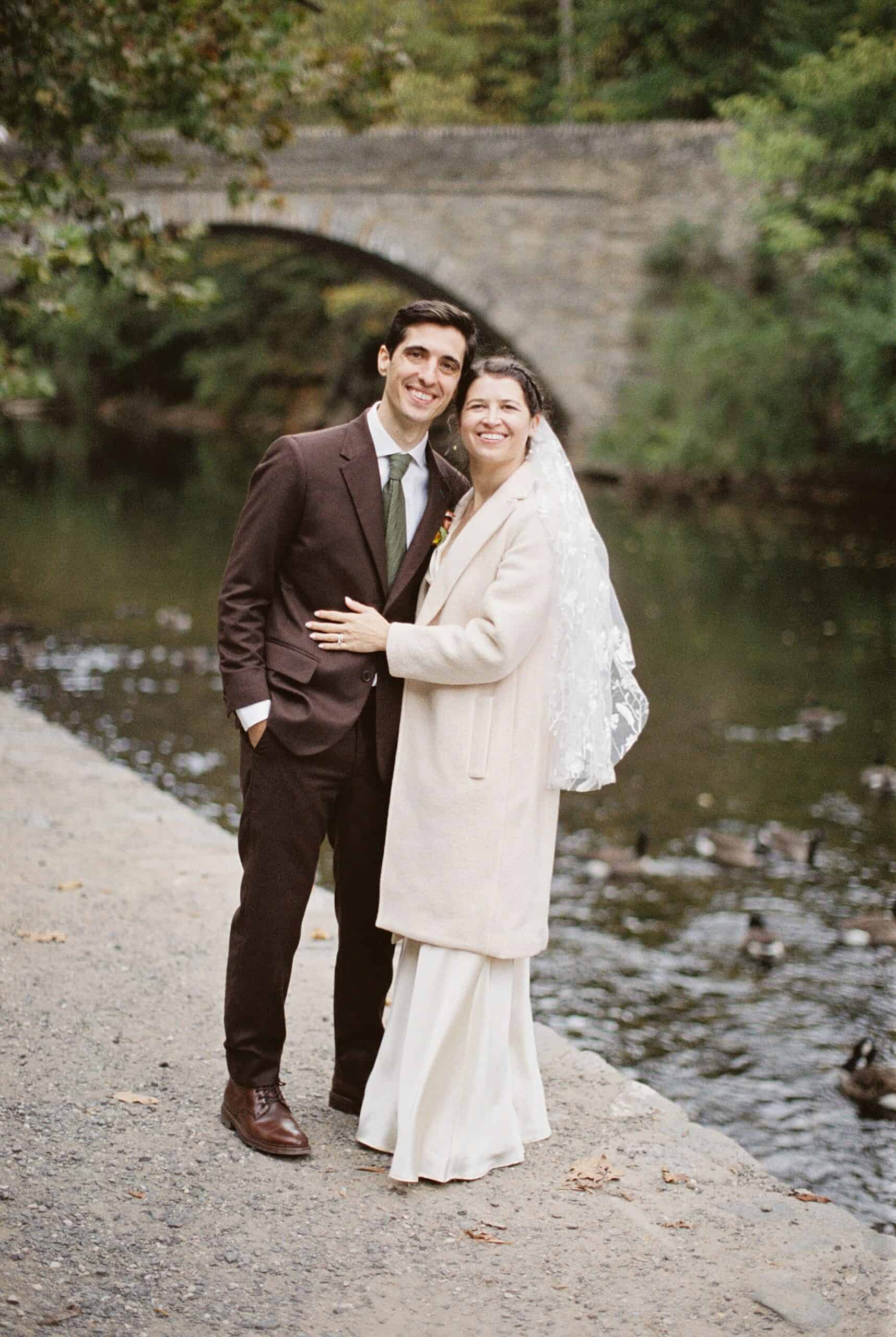 a 35mm film image of a bride and groom on their wedding day with a beautiful creek, bridge and swimming geese in the background