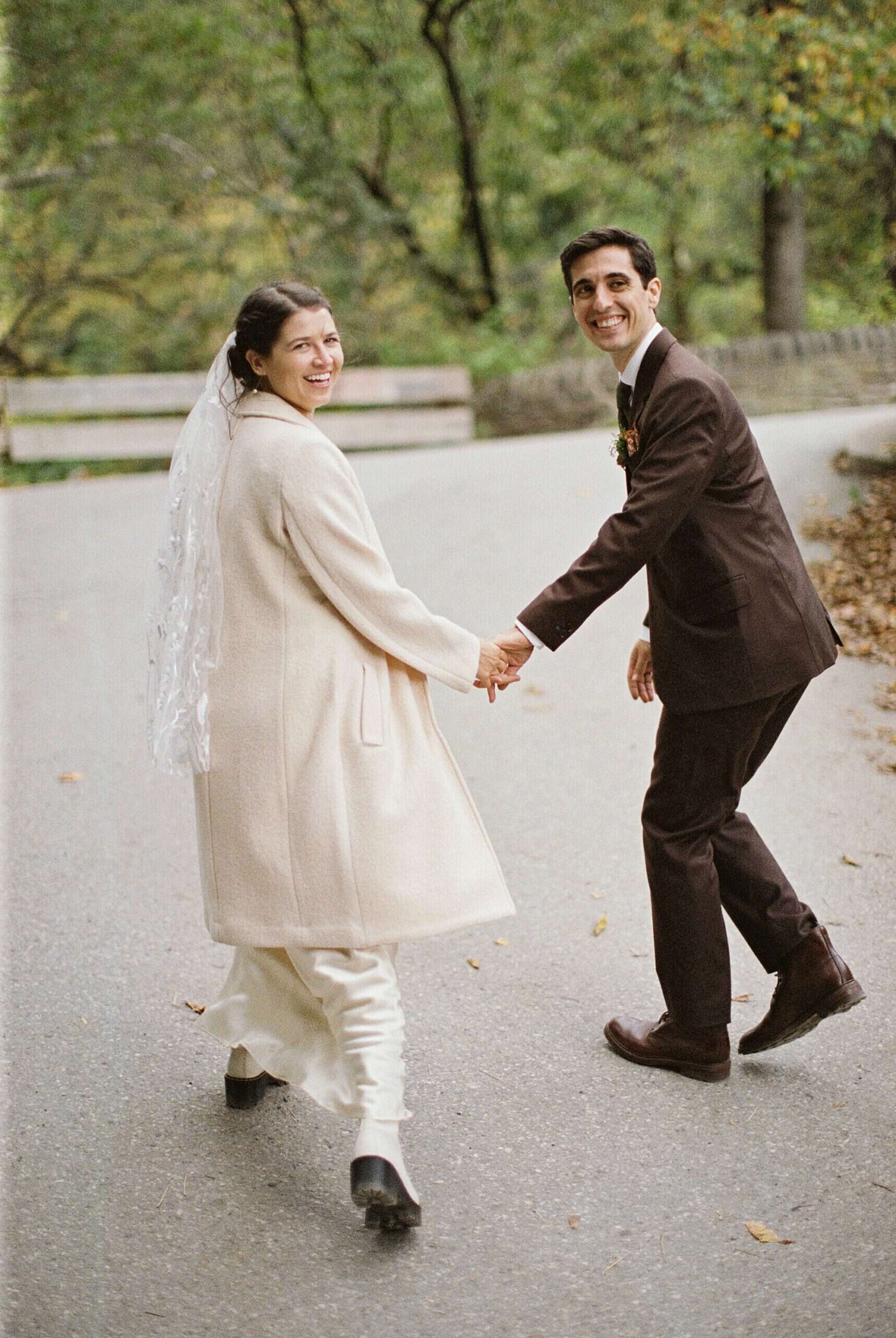 a film photography image of a bride and groom walking down a stone path  and smile back at the camera