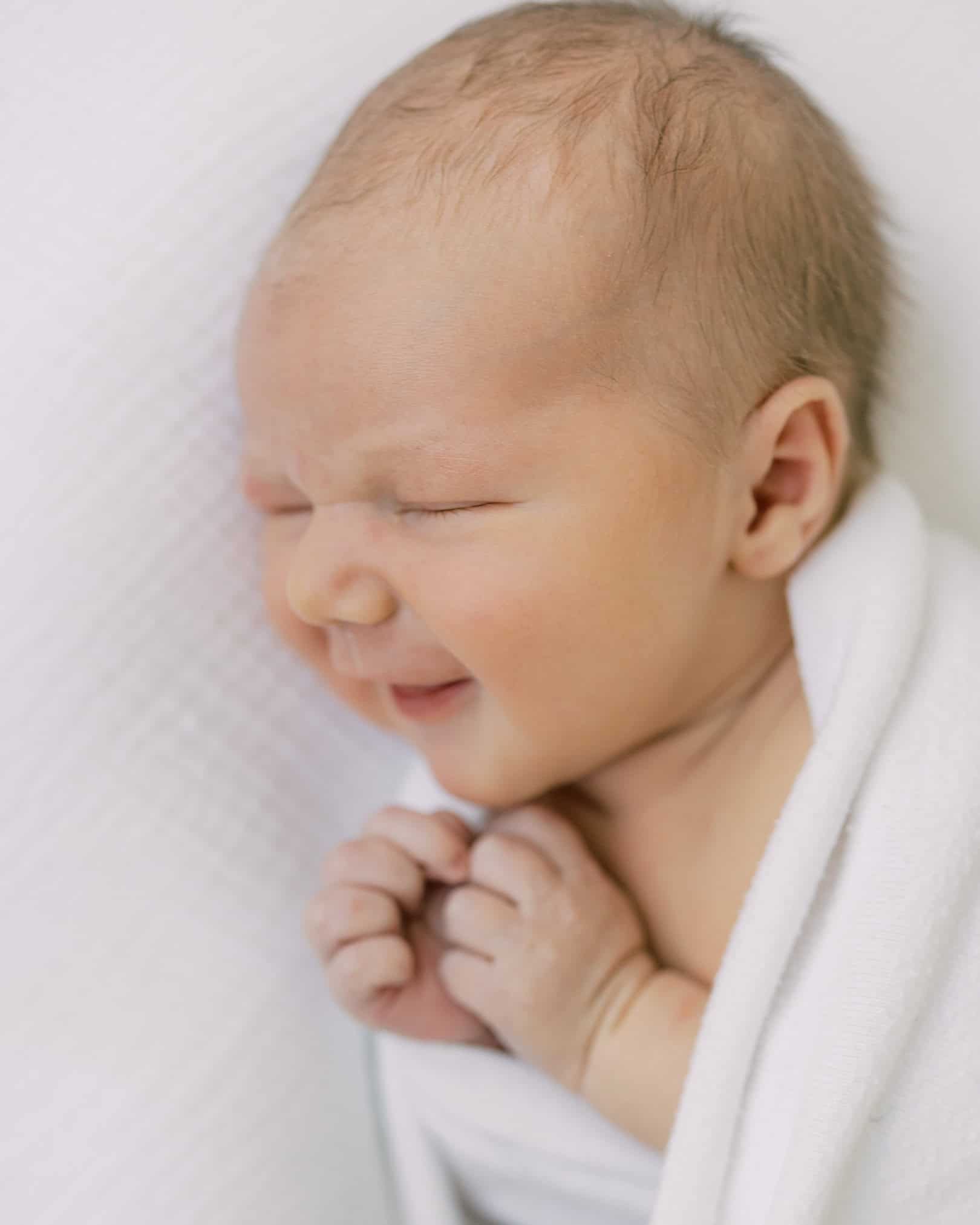 a close up portrait of a smiling newborn baby on a white backdrop