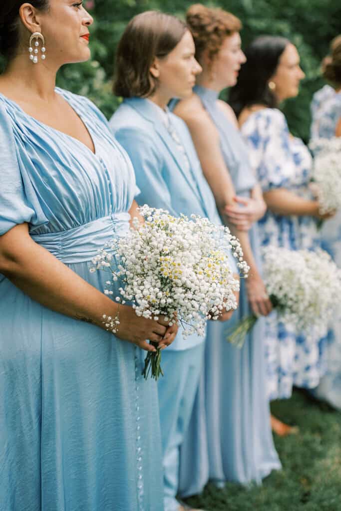 Bridesmaids in soft blue dresses holding baby’s breath and chamomile floral bouquets during a wedding at Tyler Arboretum in Philadelphia.