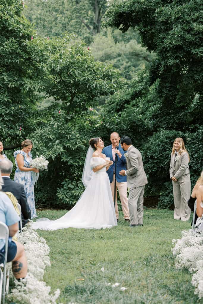 Bride and groom laughing together during their outdoor ceremony beneath the trees at a wedding at Tyler Arboretum in Philadelphia.