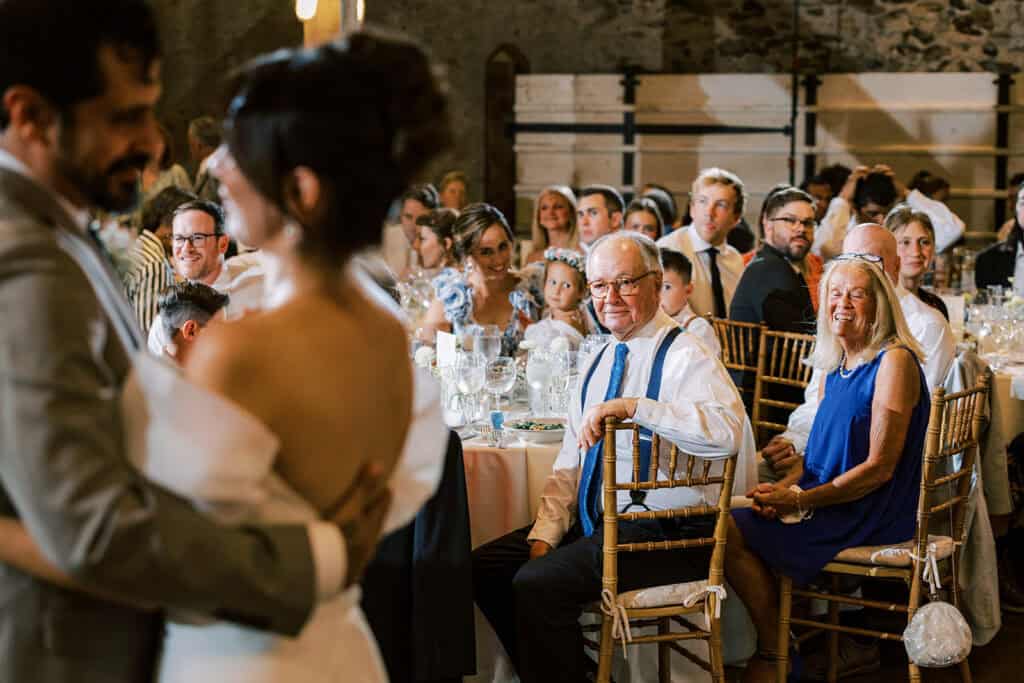 Guests smiling and watching the couple’s first dance during a wedding reception at Tyler Arboretum in Philadelphia, with gold Chiavari chairs and candlelit table settings in the background.