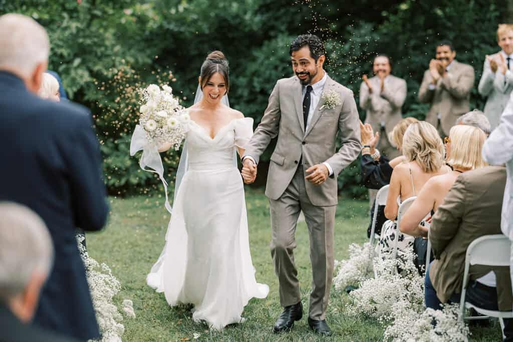Bride and groom walking up the aisle through rows of baby’s breath florals after being pronounced married at a wedding at Tyler Arboretum in Philadelphia.