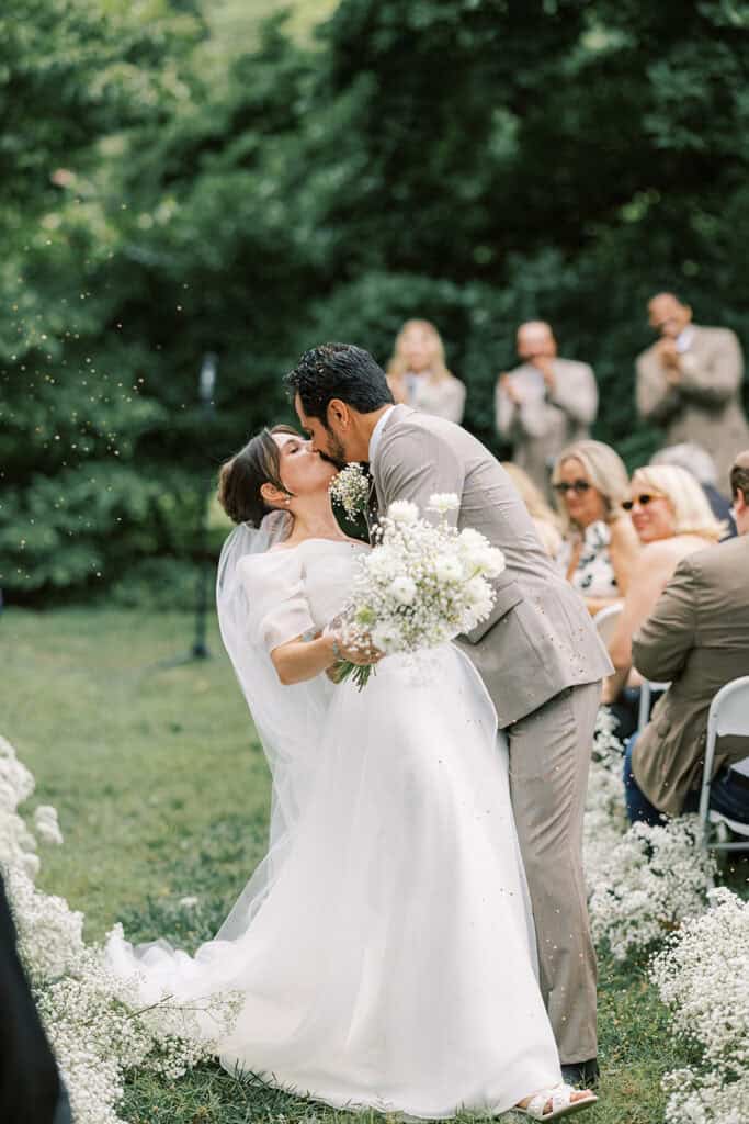 Bride and groom sharing a joyful kiss surrounded by floating confetti and baby’s breath aisle florals at their outdoor wedding at Tyler Arboretum in Philadelphia.