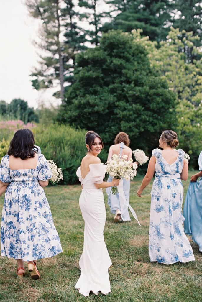 Bride walking with her bridesmaids across the gardens at Tyler Arboretum in Philadelphia, carrying a bouquet of white daisies, chamomile, and baby’s breath during a wedding at Tyler Arboretum.