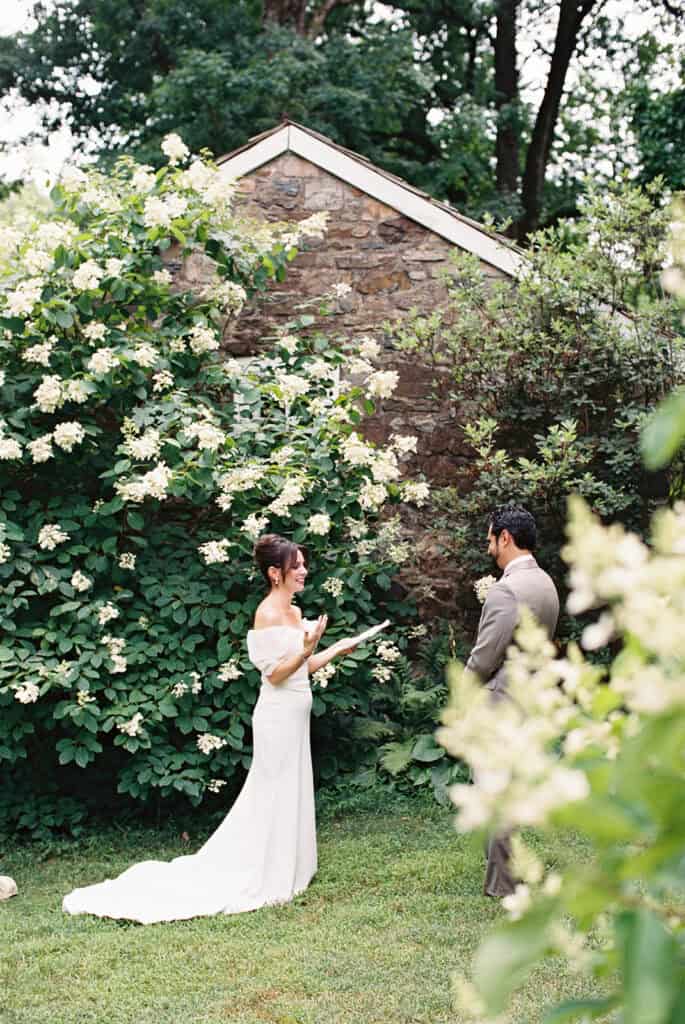 Bride and groom exchanging private vows in a secluded garden alcove surrounded by hydrangeas and stone walls during their wedding at Tyler Arboretum in Philadelphia.