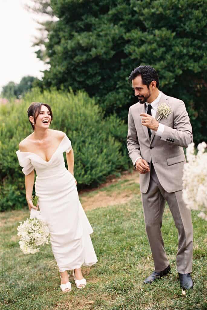 Bride and groom laughing together in the gardens at Tyler Arboretum in Philadelphia, holding baby’s breath bouquets during their wedding portraits.