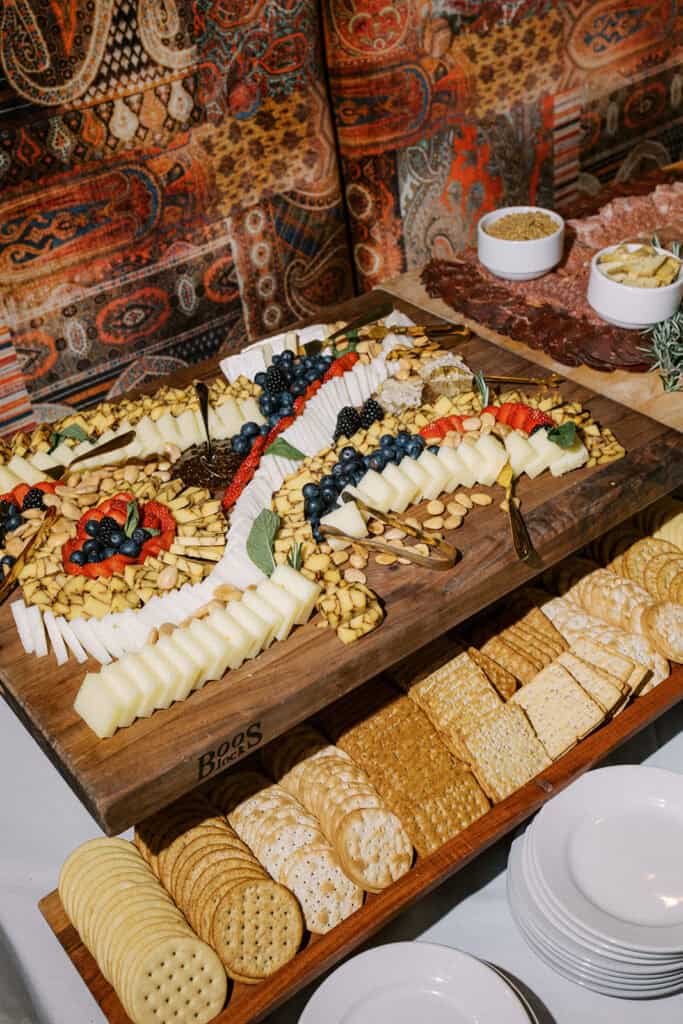Close-up of a large cheese and charcuterie display at Autograph Brasserie featuring sliced cheeses, crackers, berries, and meats during a wedding rehearsal dinner celebration.