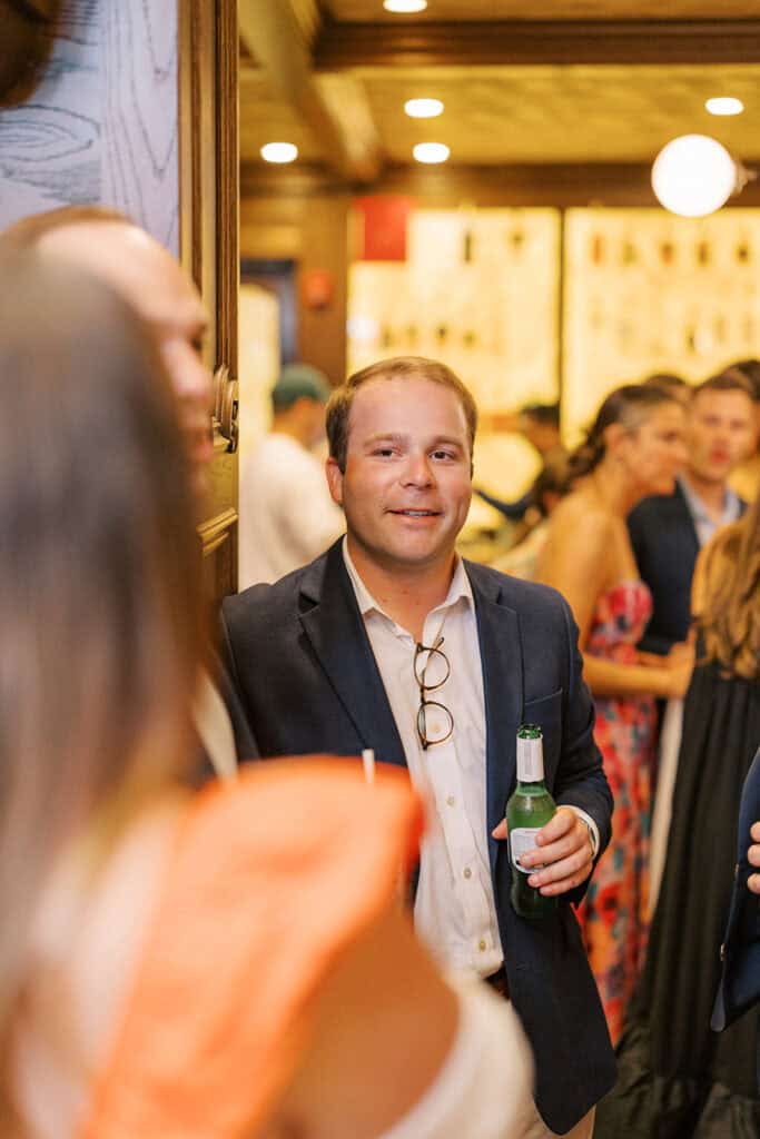 Candid photo of a wedding guest holding a beer and smiling during cocktail hour at Brenna and Fran’s rehearsal dinner at Autograph Brasserie in Wayne, Pennsylvania.