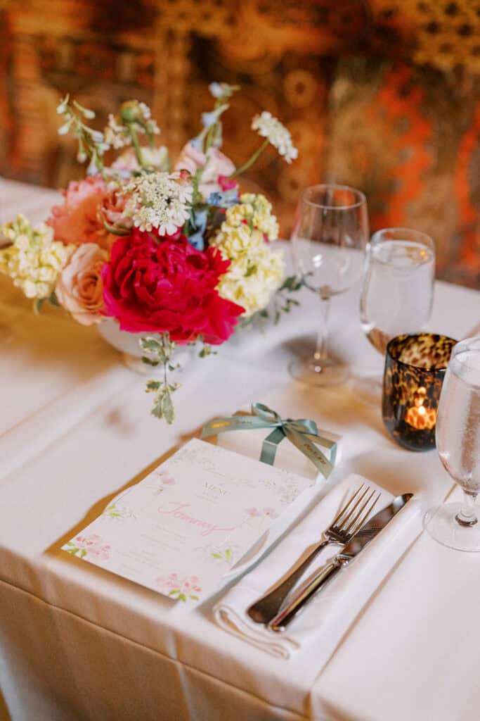Rehearsal dinner table at Autograph Brasserie with colorful floral centerpiece, blush and bright blooms, custom menu card, candlelight, and place setting for a spring wedding weekend in Pennsylvania.