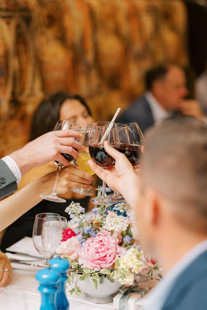 Guests clinking wine glasses over a table with colorful spring florals during Brenna and Fran’s rehearsal dinner at Autograph Brasserie, capturing an intimate pre-wedding celebration moment.