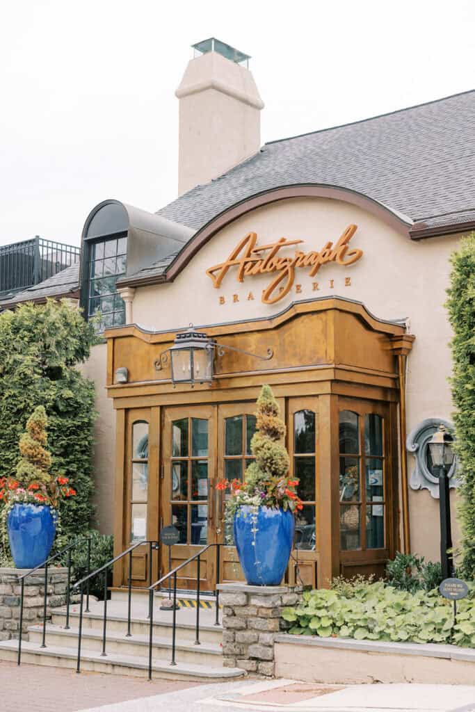 Exterior of Autograph Brasserie in Wayne, Pennsylvania photographed during Brenna and Fran’s wedding rehearsal dinner, featuring the restaurant’s entrance, wood doors, and blue ceramic planters.